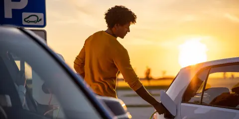 Person plugging an electric car into a charging station in a parking lot