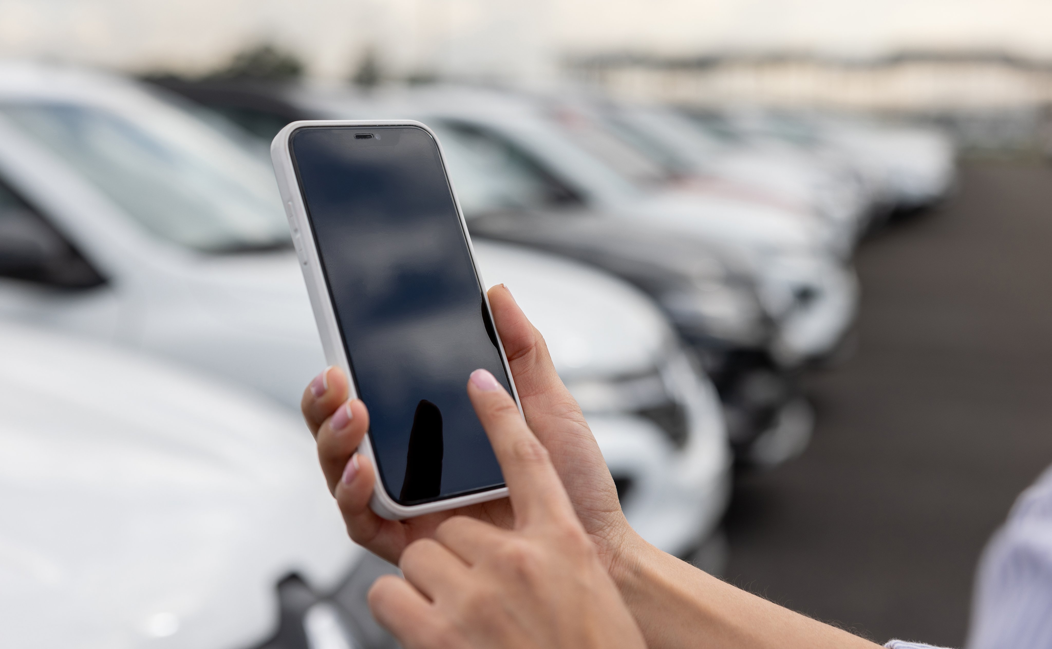 Close-up on a woman using a mobile app on her smartphone at a car dealership
