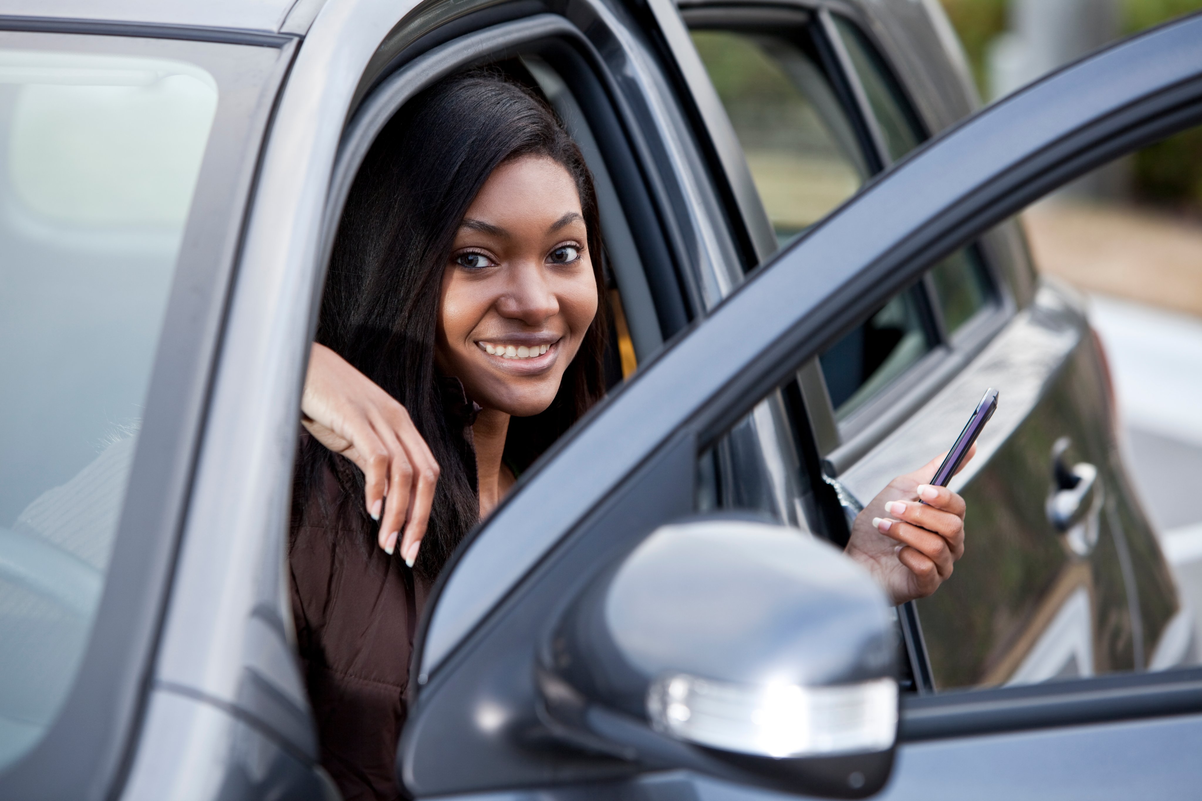 Teenager, 17 years, sitting in driver’s seat of car holding mobile phone