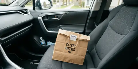 Paper takeout bag labeled sitting on the front passenger seat of a car