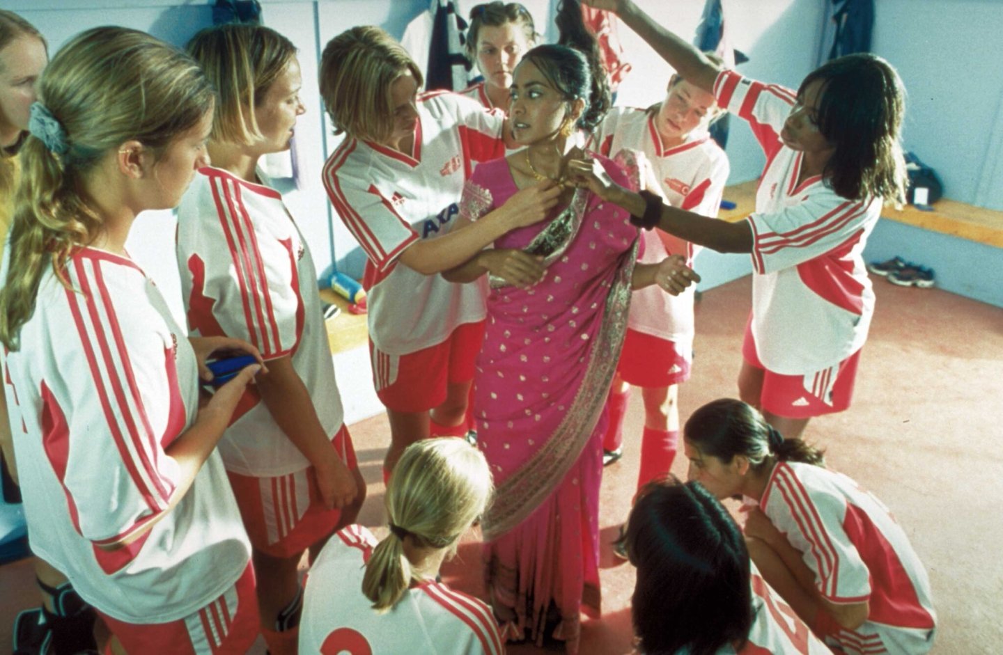 Scene of girl's uniformed soccer team surrounding a friend who is wearing a traditional sari.