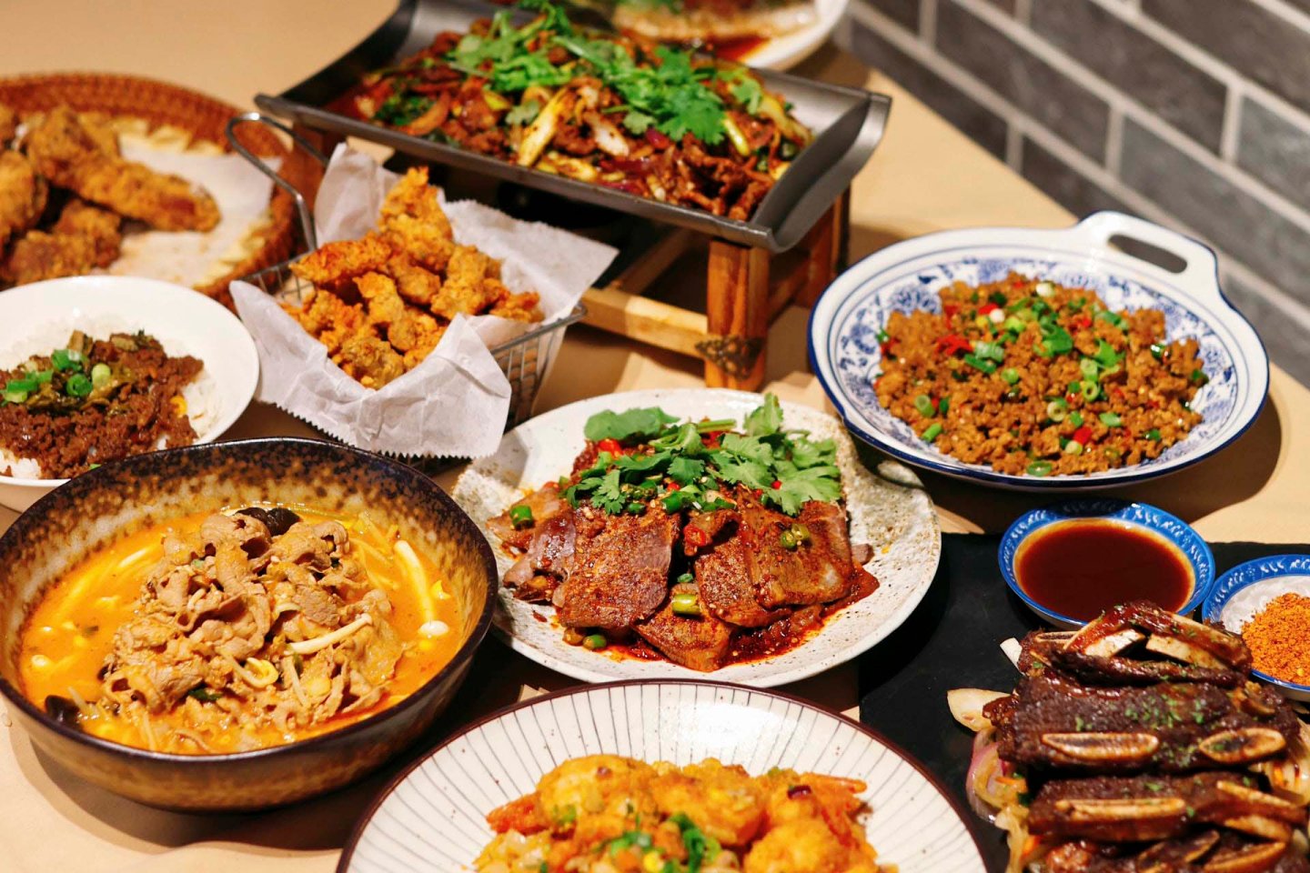 A table filled with various Asian dishes, including sliced meat in rich orange sauce, fried chicken bites, stir-fried vegetables with herbs, a dish of cooked ground meat with peppers, and grilled meat on a platter, all garnished with cilantro.