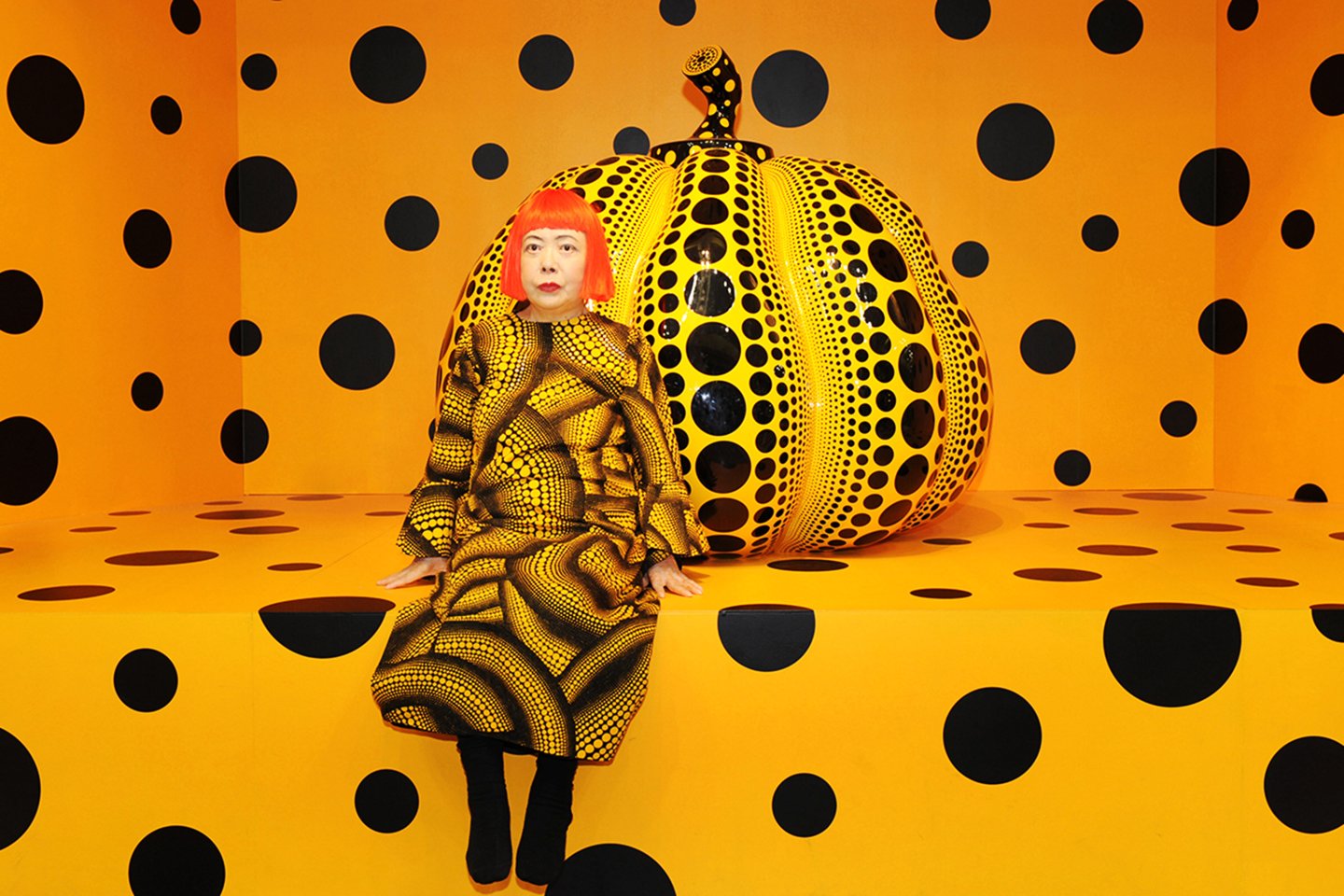 Photo of Yayoi Kusama sitting with one of her iconic pumpkins.