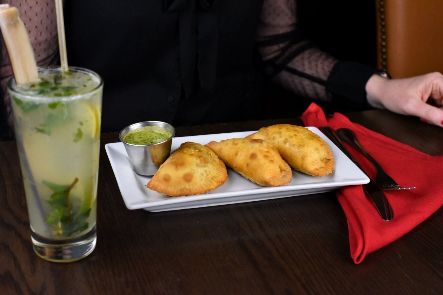 a mojito on a table with a plate of empanadas
