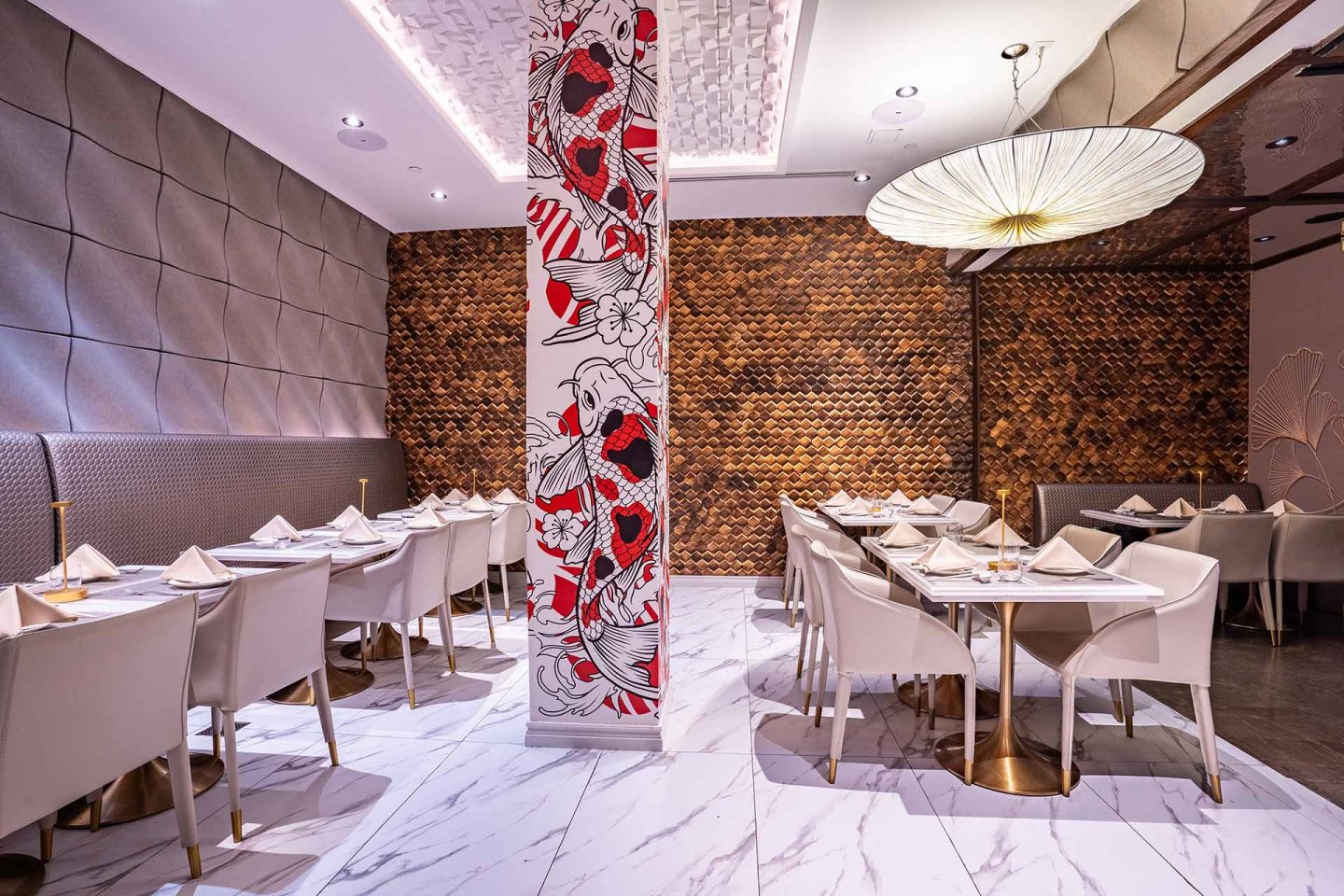 Modern restaurant interior with white marble floors, white chairs and tables set for dining, a decorative column with red and black floral art, textured walls, and a large round hanging light fixture.
