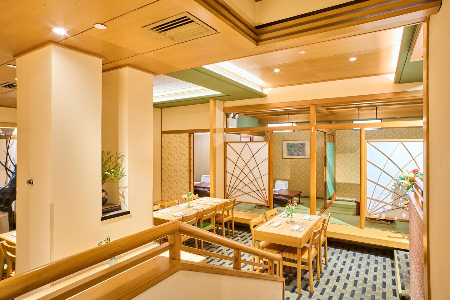 A spacious Japanese restaurant interior with wooden tables, chairs, and decorative partition screens. Soft lighting, plants, and minimalist decor create a calm, inviting atmosphere.
