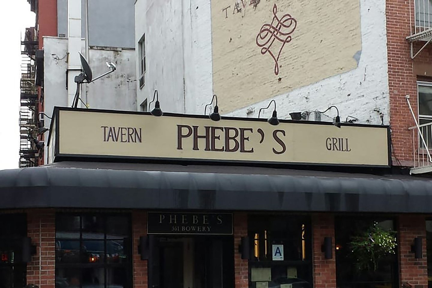 A restaurant sign reads "PHEBE'S" with "TAVERN" on the left and "GRILL" on the right. The building is brick, with windows and a black canopy. A faded mural is visible on the wall above.