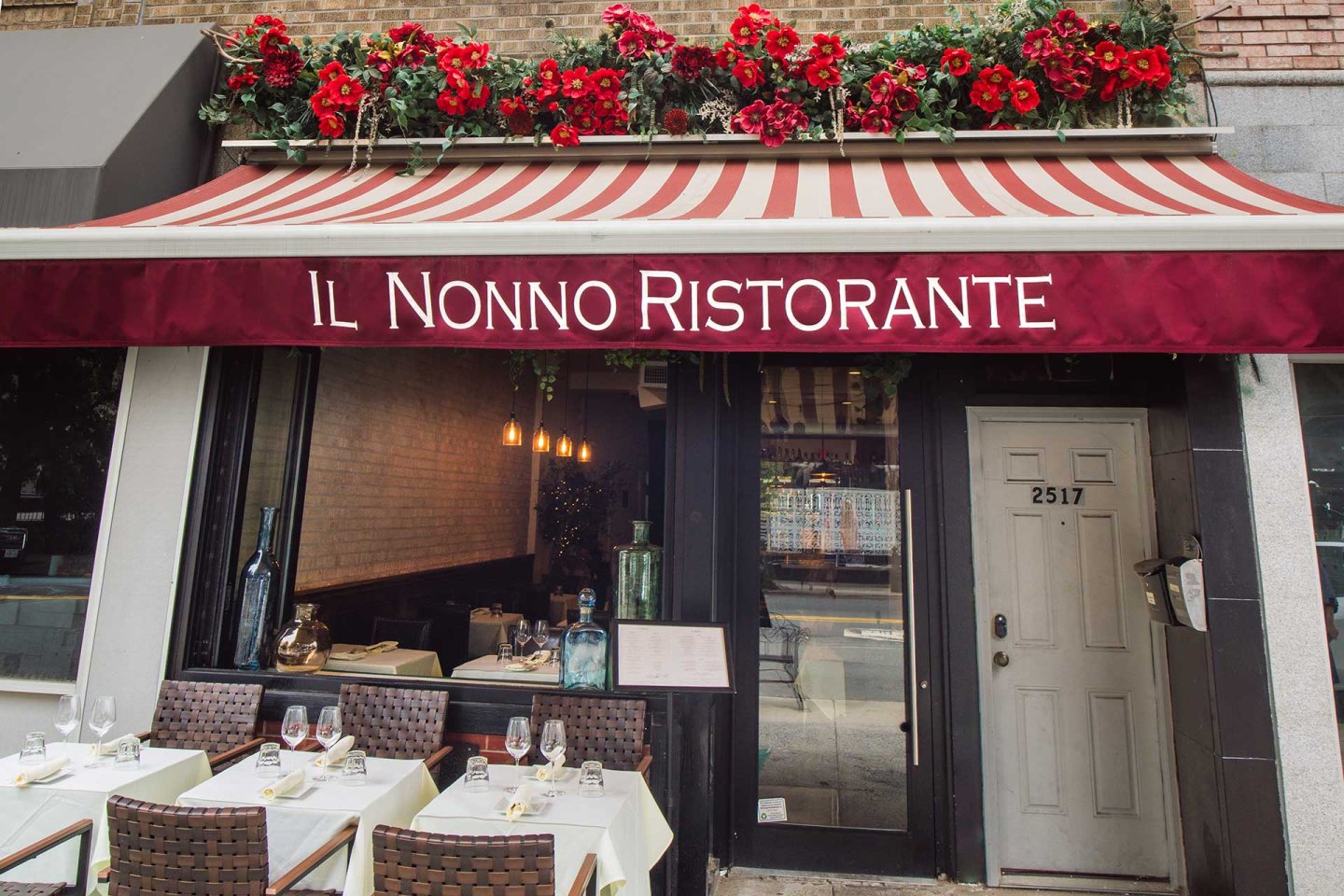 Street view of Il Nonno Ristorante with a red and white striped awning, floral decorations above, and outdoor tables set with white tablecloths, wine glasses, and wicker chairs. The address "2517" is on the door.