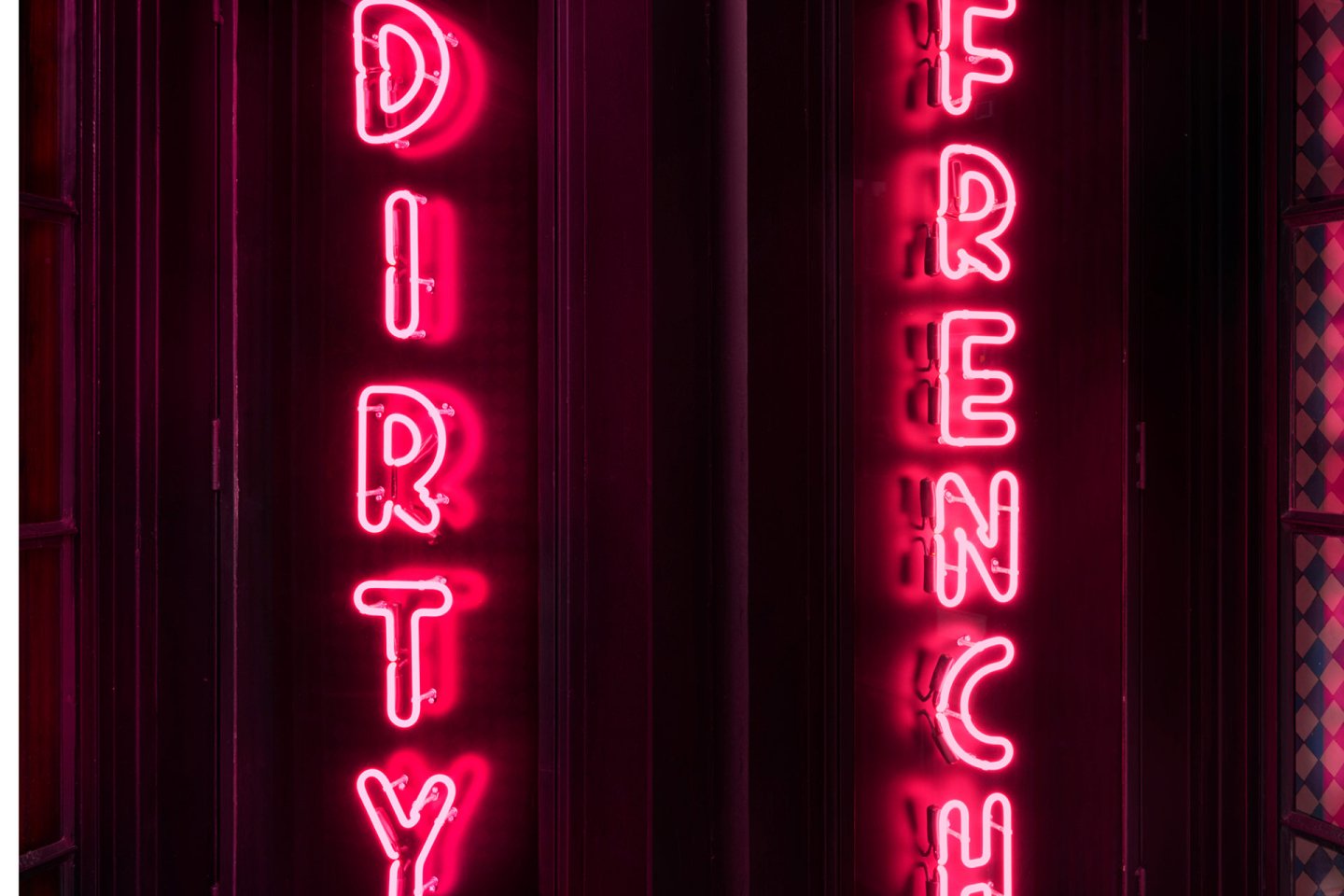 Bright pink neon signs spell out "DIRTY" and "FRENCH" vertically on a dark background, creating a bold and eye-catching display.