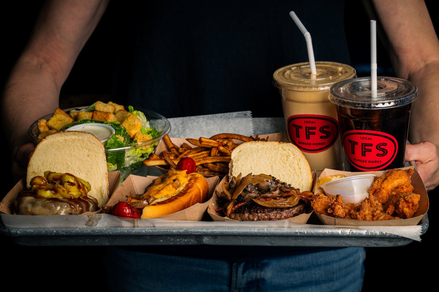 tray of food with salivating burgers, hot dog covered in grilled onions and cheddar, milkshake, salad, and hand cut Belgian style fries