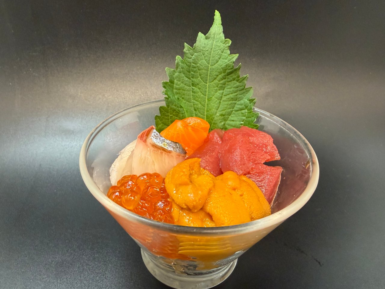 Mini chirashi seafood cup with uni, ikura, tuna, salmon, striped jack and shiso leaf.