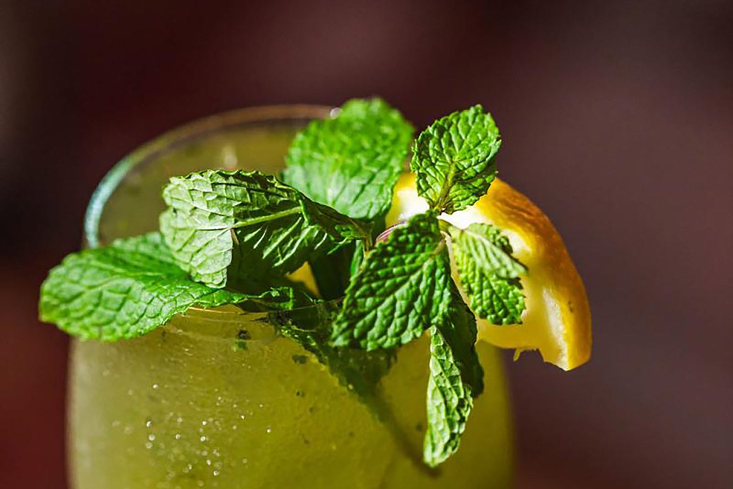 A close-up of a refreshing drink garnished with fresh mint leaves and a slice of lemon, with condensation visible on the glass.