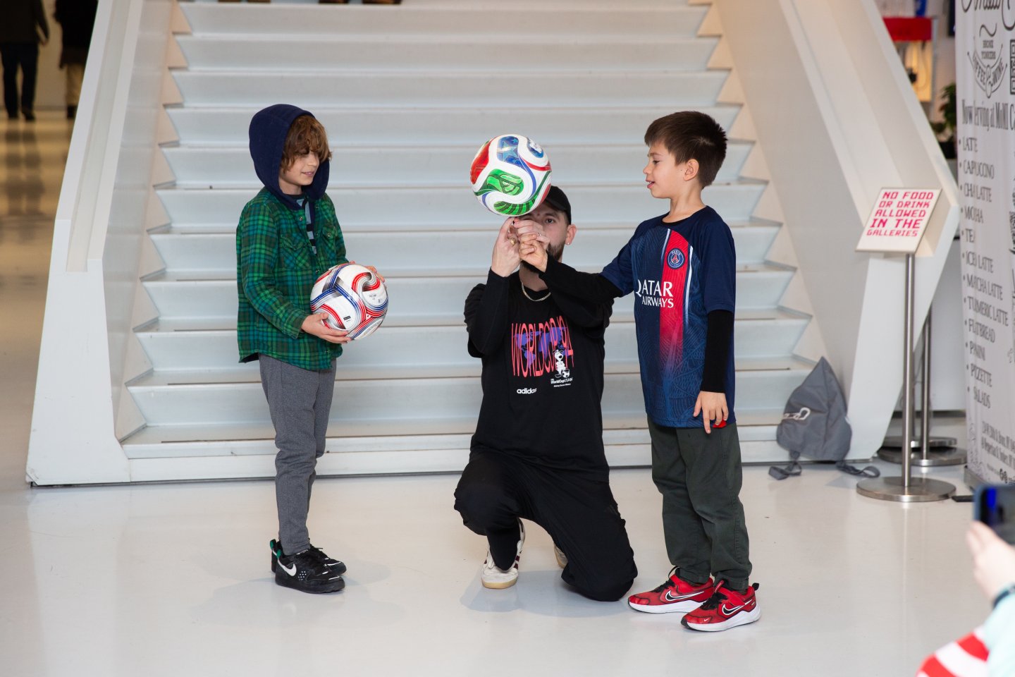 A soccer expert shows two young boys how to balance a soccer ball on a finger.