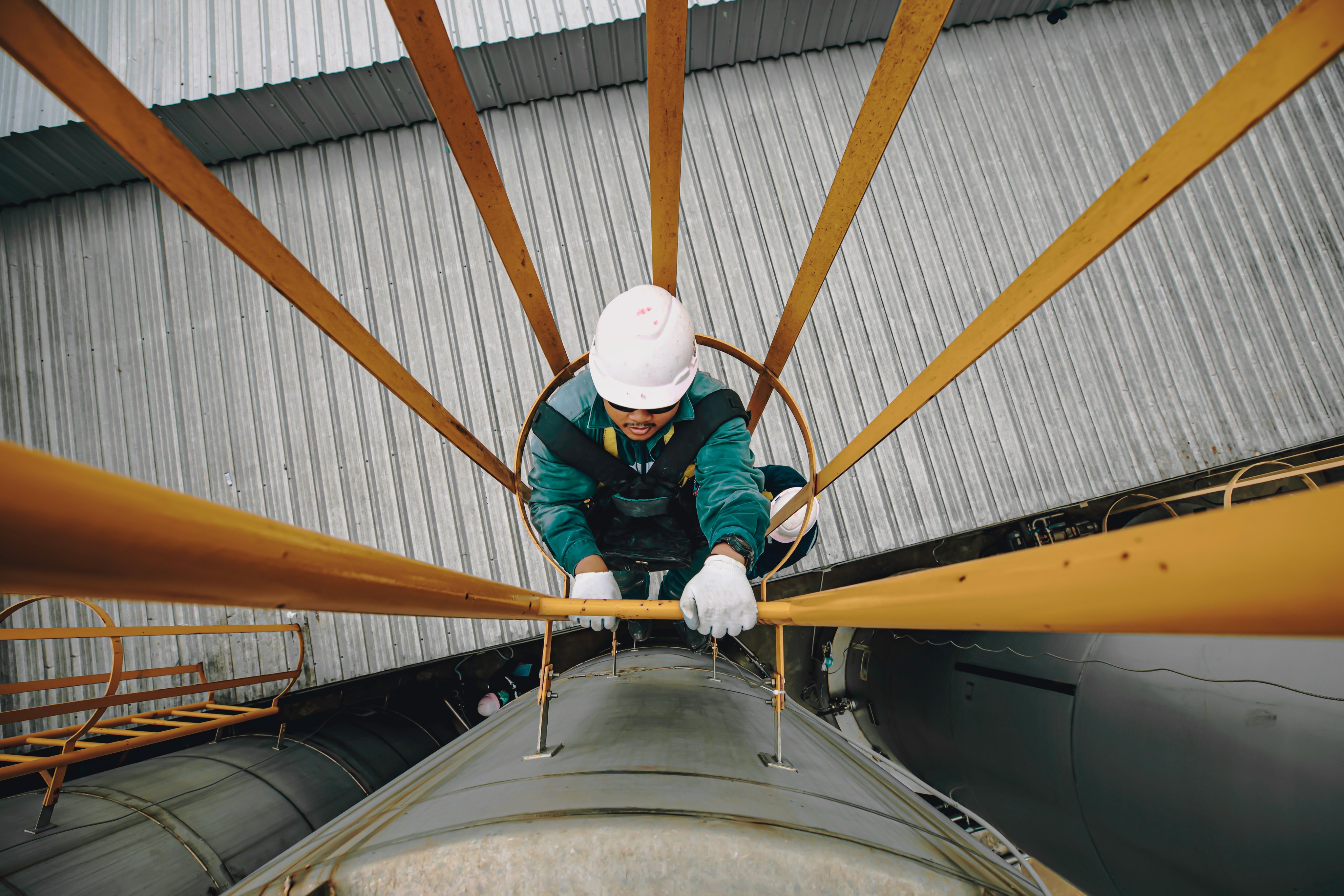 Top view male worker climbs up the ladder inspection stainless tank work at height safety harness.