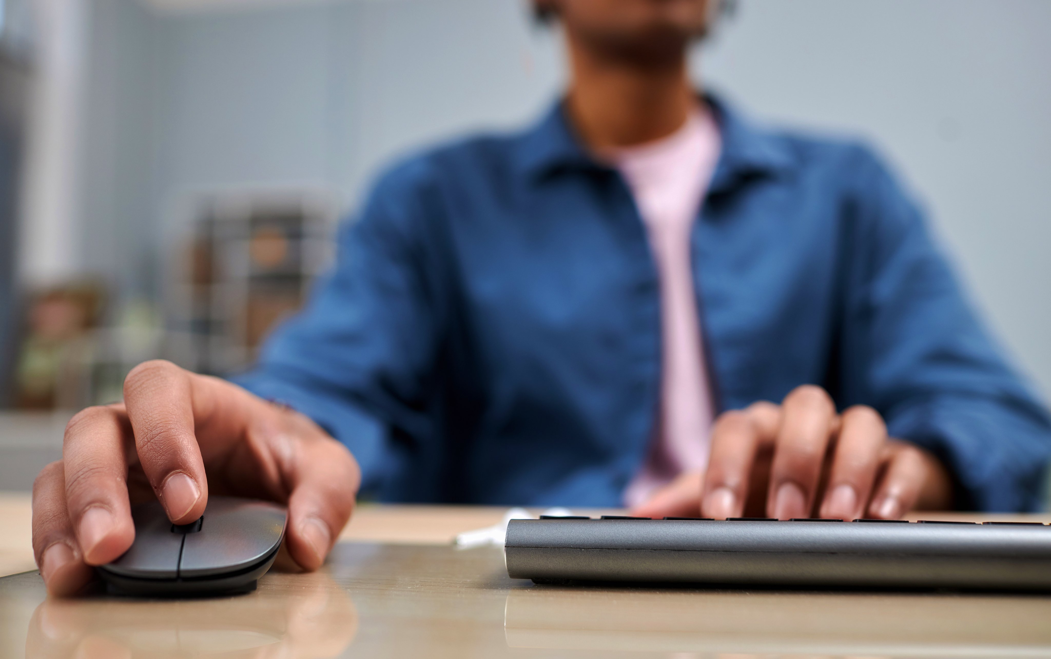 Closeup of young black man using computer at desk in college with focus on male hands typing and using mouse