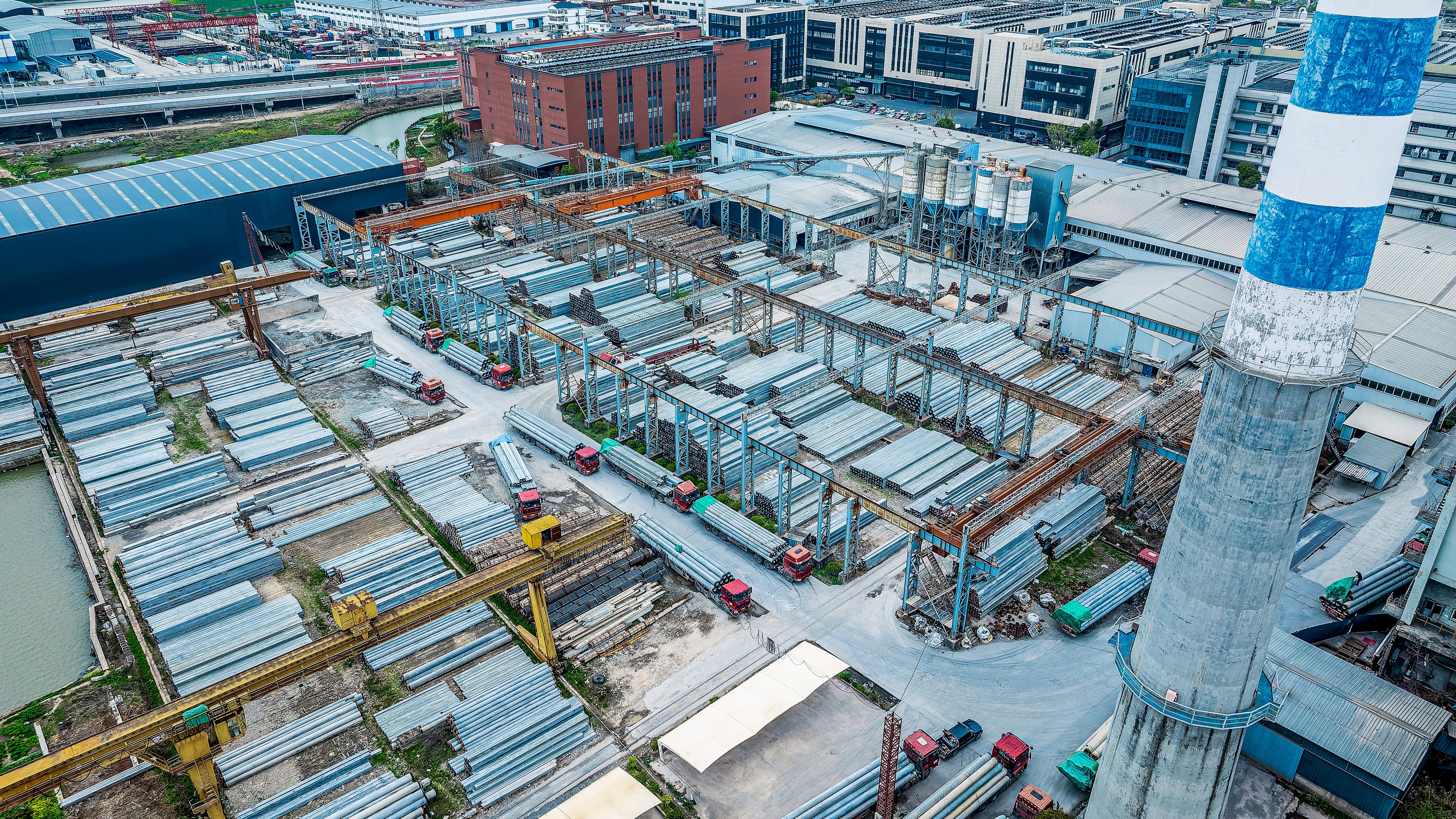 Aerial view of concrete pipe factory yard with tall chimney.