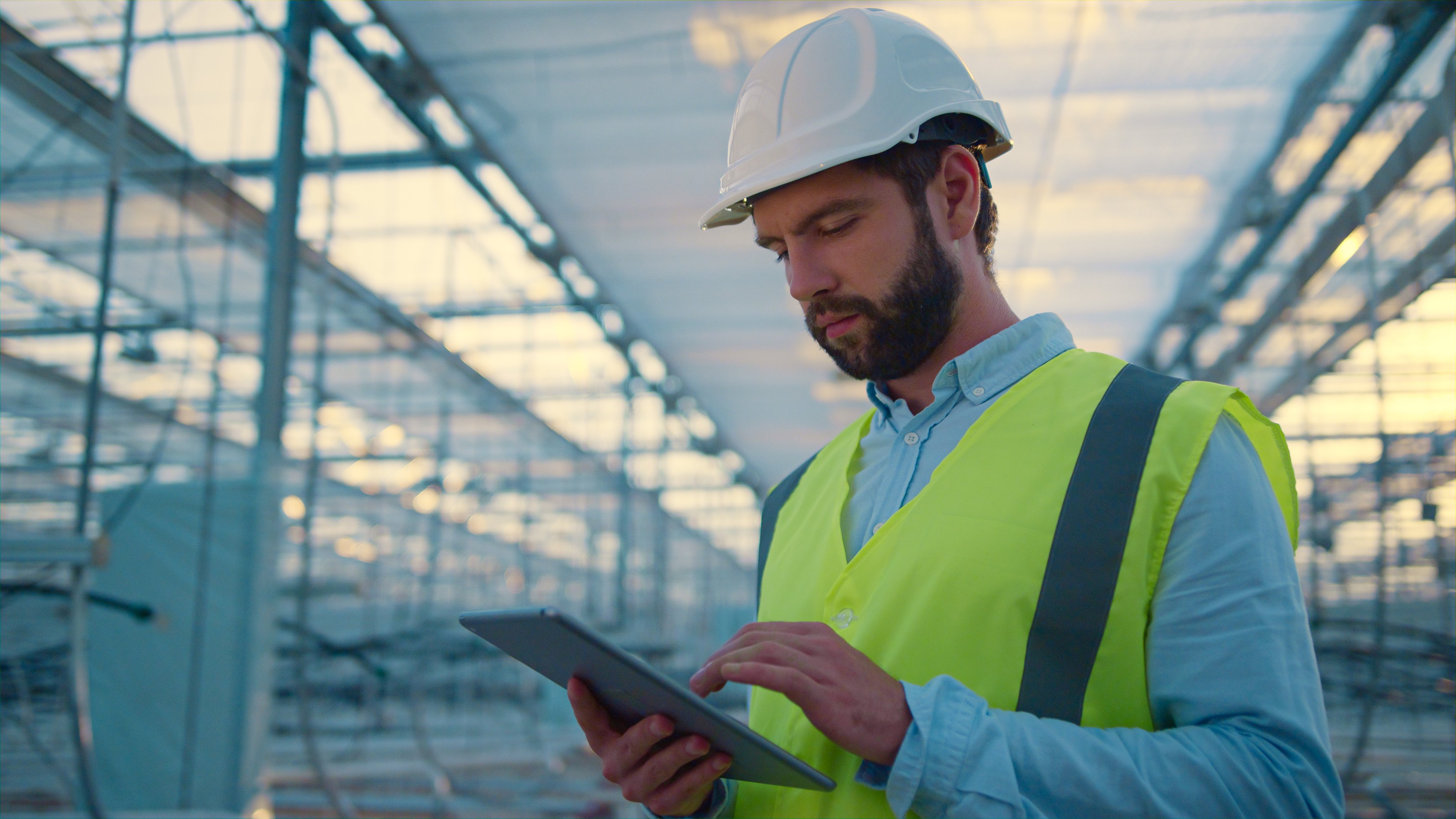Factory worker with tablet inspecting new manufacture wearing green uniform. Handsome caucasian man production expert analysing important manufacturing information. Engineering occupation concept