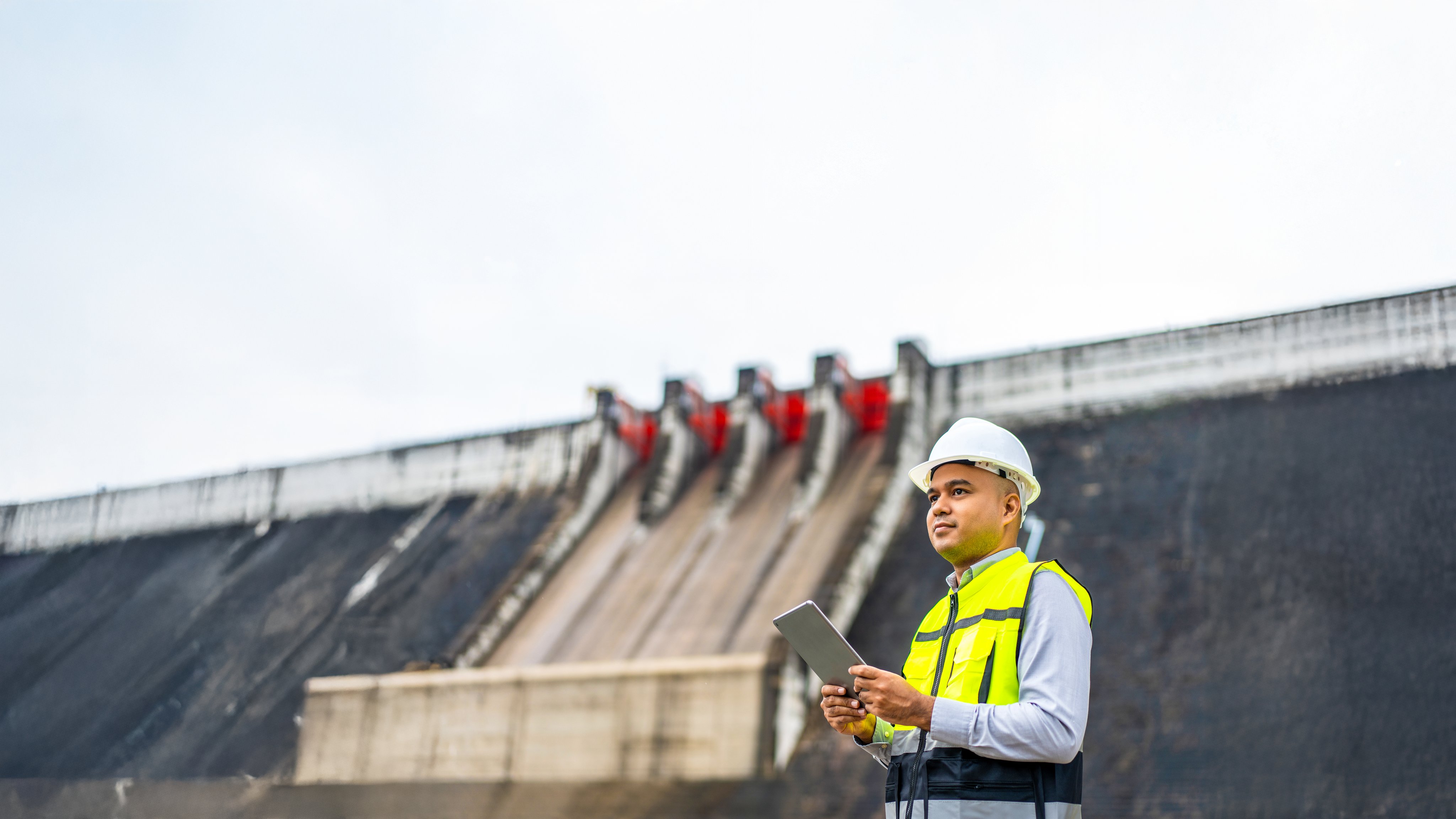 Professional asian maintenance engineer man with safety helmet in construction site dam with hydroelectric power plant and irrigation. Manager engineer man working with tablet at project big building.