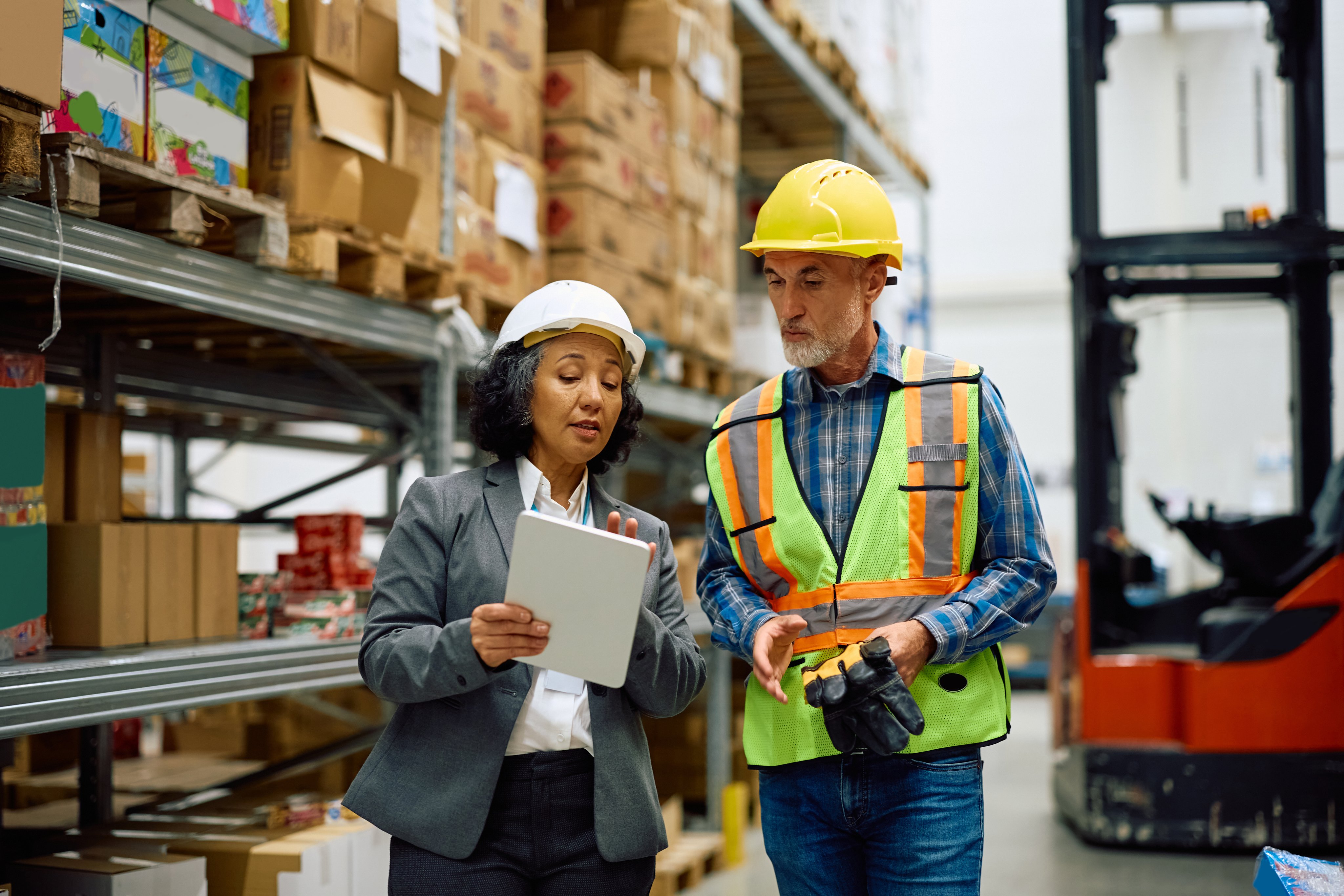 Female warehouse manager and a worker cooperating while using digital tablet in storage room. 