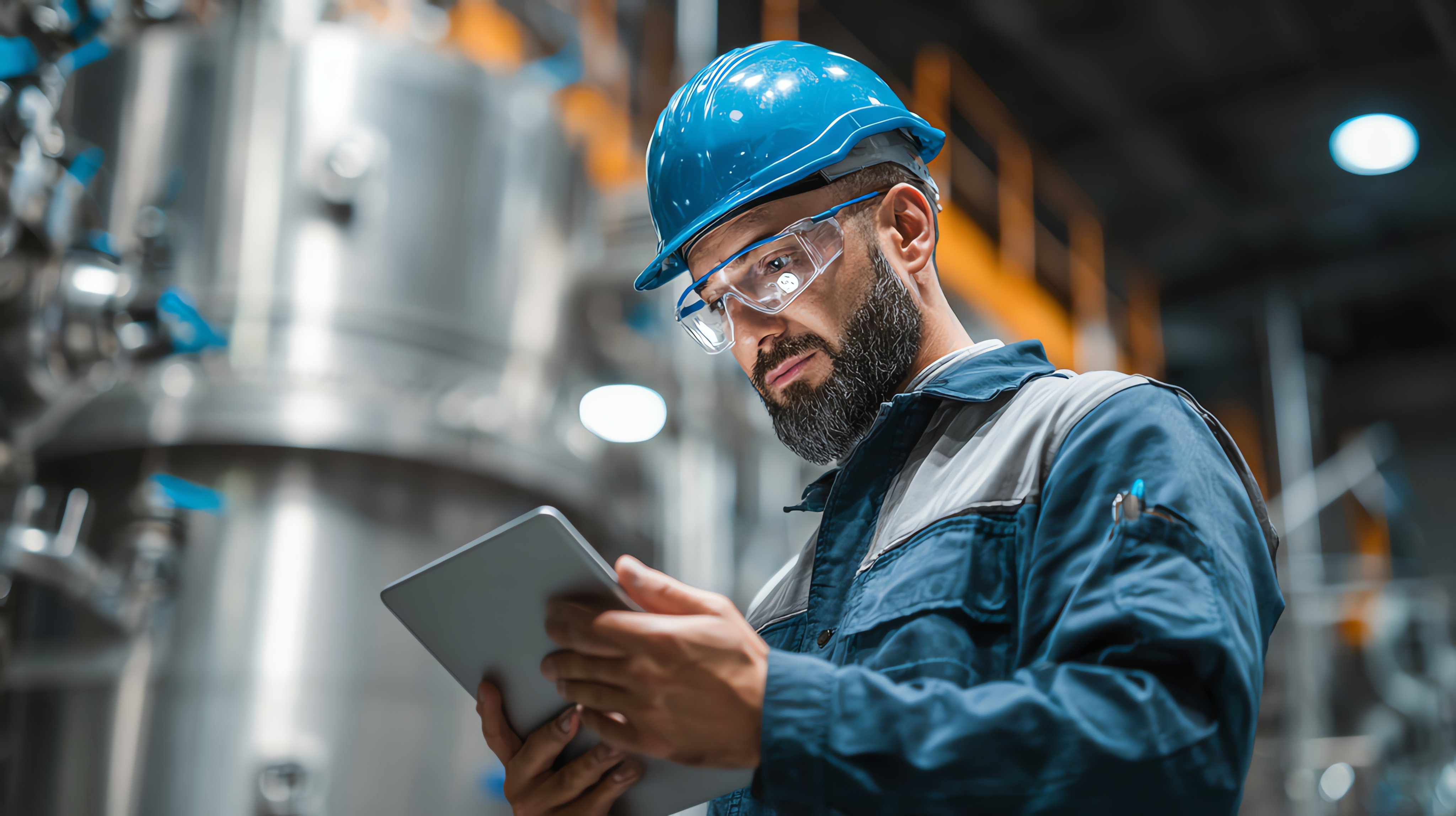 Industrial quality control officer wearing helmet and safety glasses inspecting machinery with tablet in the plant test lab