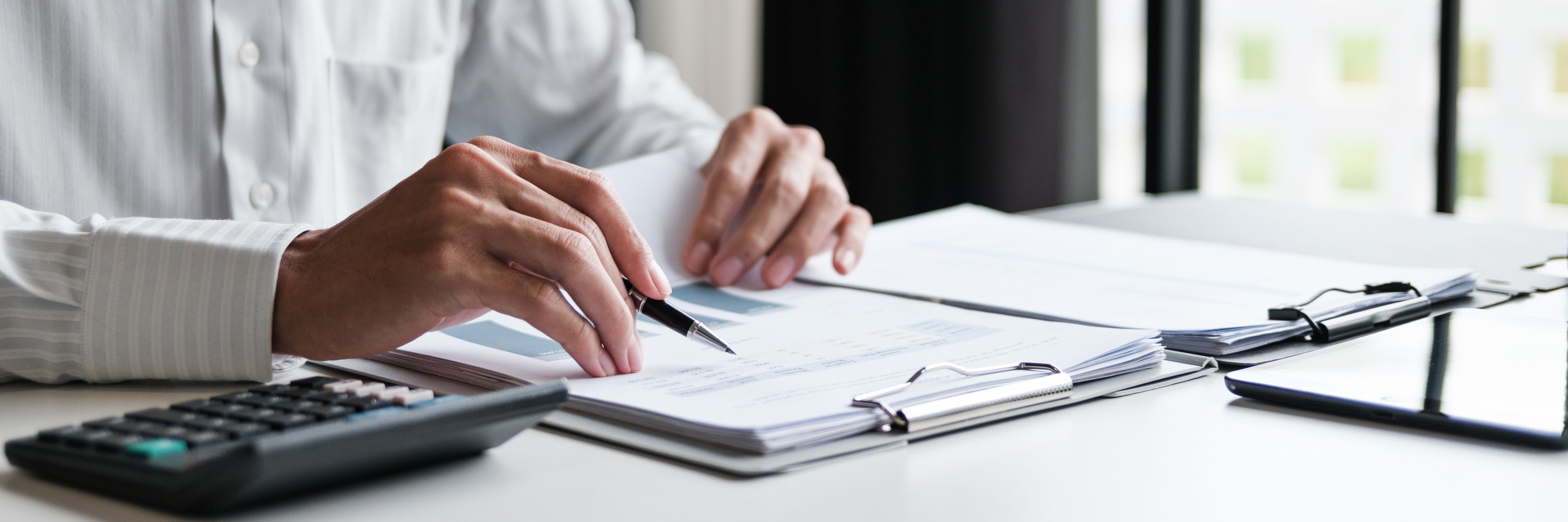 Office administrator reviewing audit documents on table with calculator and financial file folders