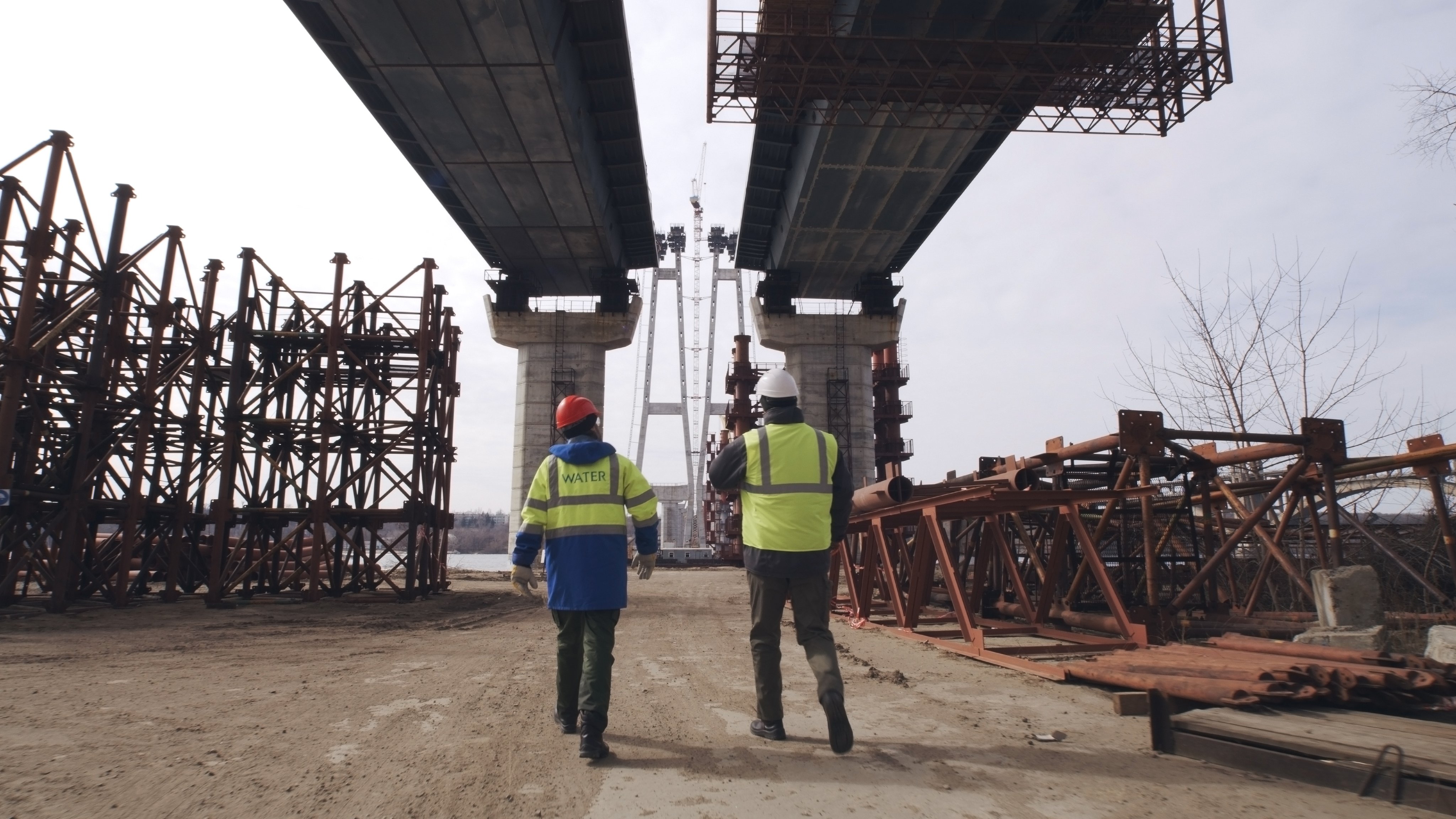 Anonymous men in uniform walking under bridge during work on construction site