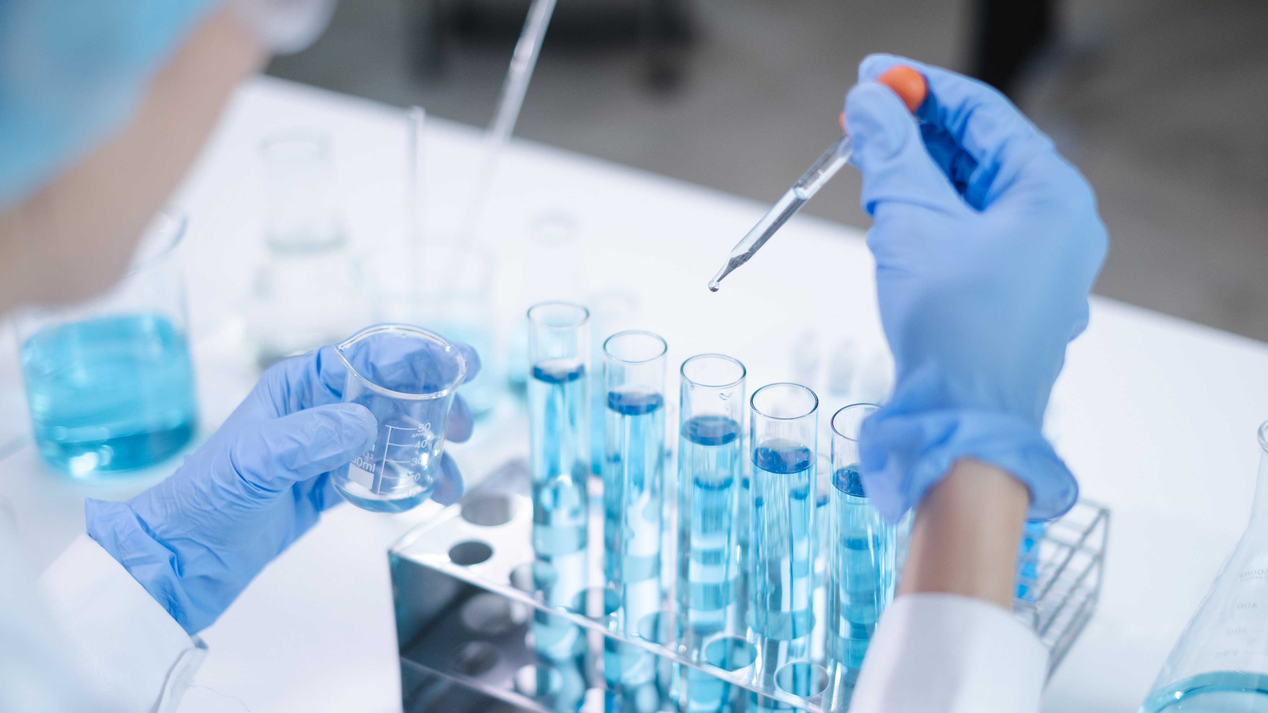 Close-up hands dropping fluid from dropper flask beaker into blue test tube sample laboratory for compare in medicine chemical biology medical science experiment technology biotechnology analysis