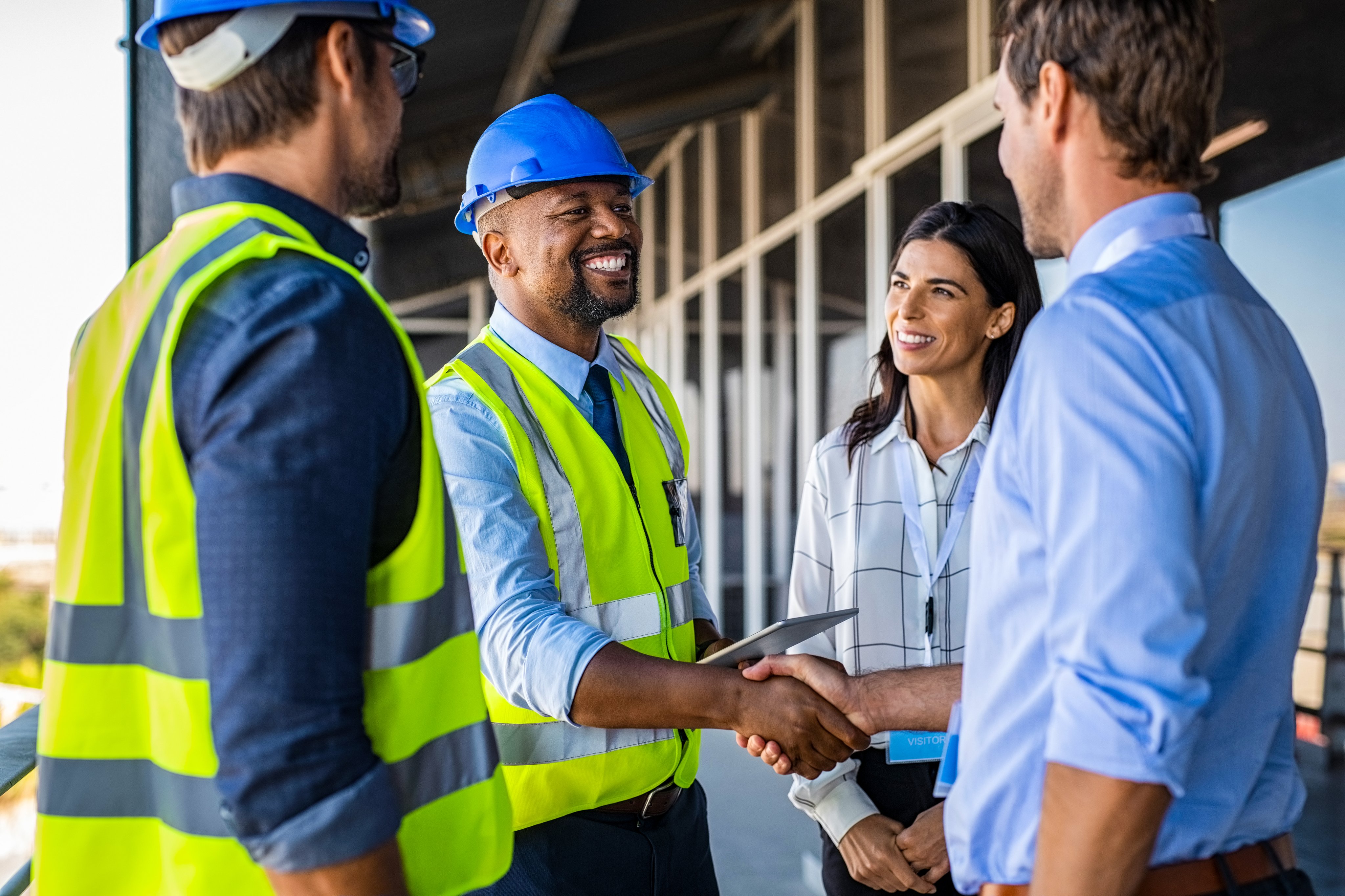 Smiling engineer shaking hands at construction site with happy architect. Handshake between cheerful african construction manager with businessman at bulding site. Team of workers with architects and contractor conclude an agreement with safety uniform.