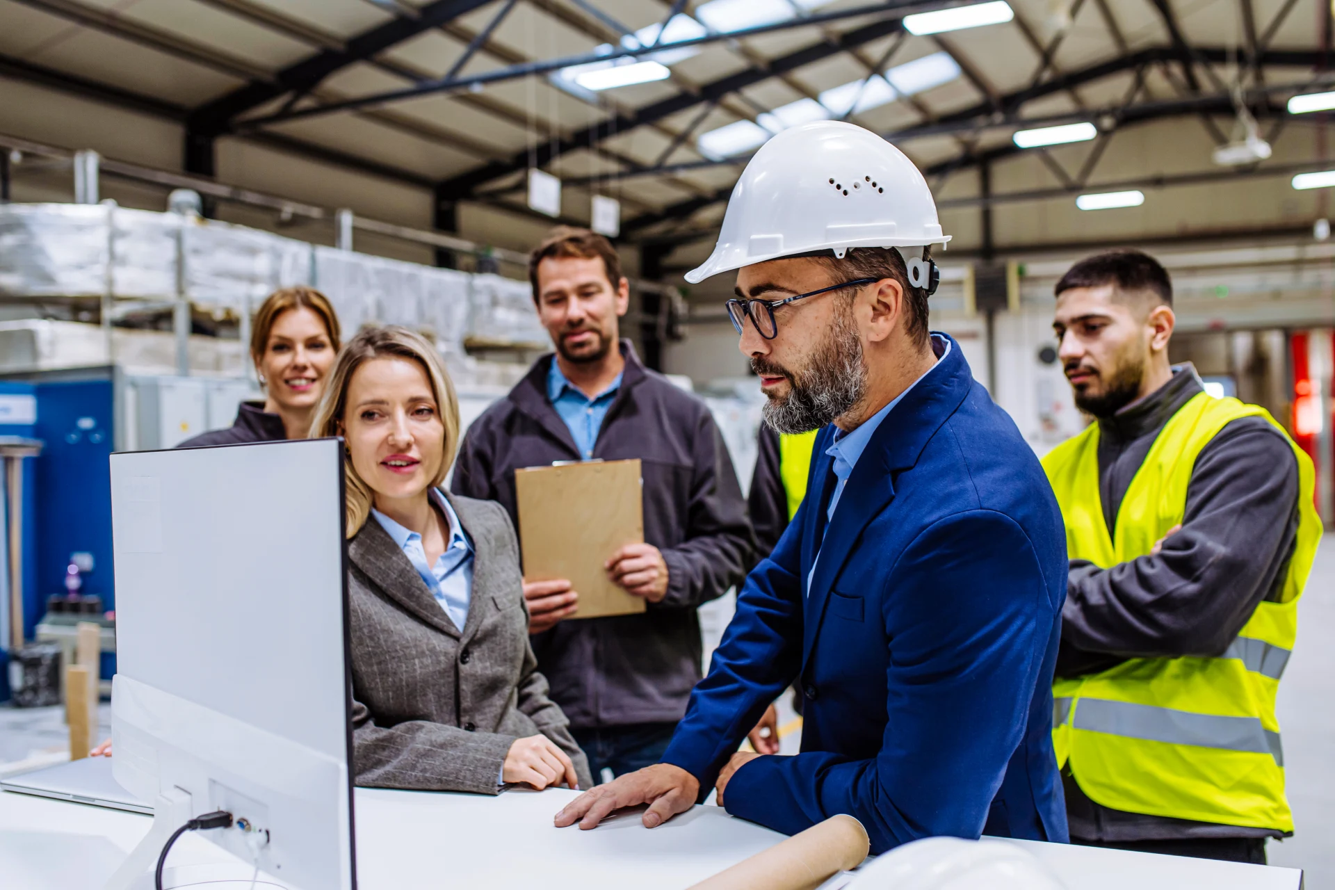 Manager presenting project to the full team of warehouse employees on computer. Team of workers, managers, female director in modern industrial factory, heavy industry, manufactrury.