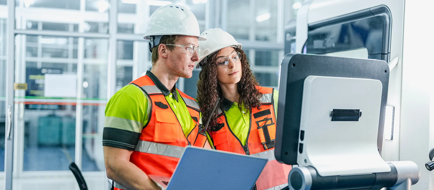 Engineers use a laptop to program an AI system for an industrial robot. The team is in a smart factory cleanroom, working on a high-tech microchip manufacturing line.