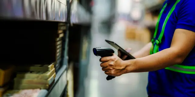 A man in a blue shirt is using a barcode scanner to scan a product. Concept of efficiency and productivity, as the man is using technology to quickly and accurately identify the product