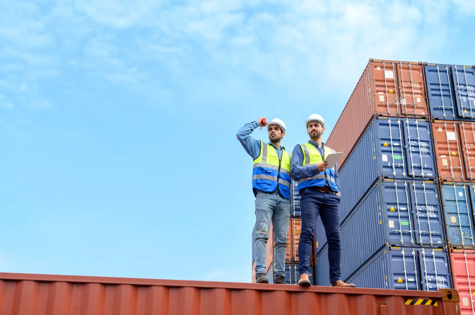 Container operator wearing white helmet and reflection shirt and holding tablet doing routine inspection while working in container yards. Logistics and shipping concept