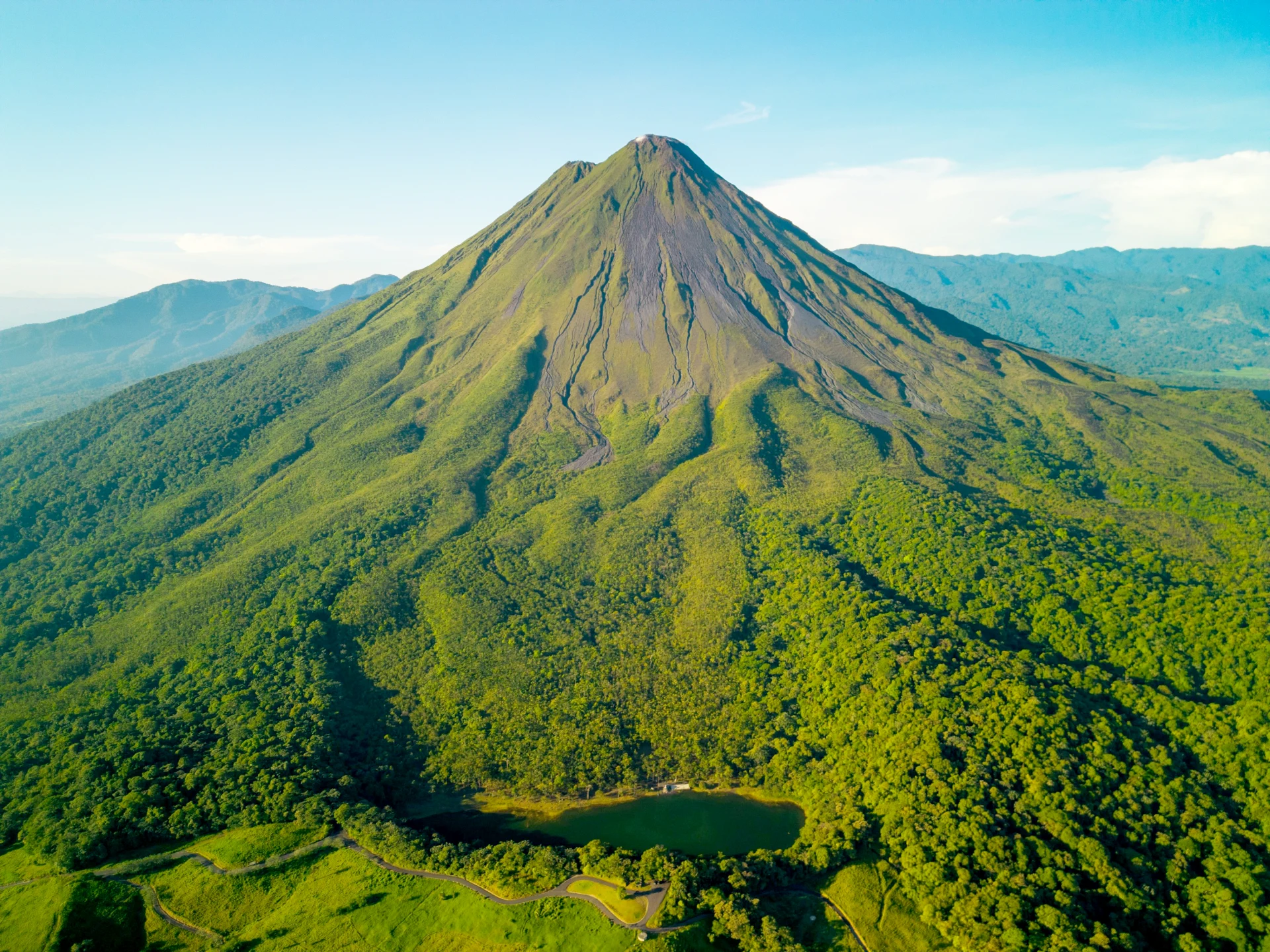 Aerial view of Arenal Volcano in Costa Rica surrounded by lush green forest under a clear blue sky