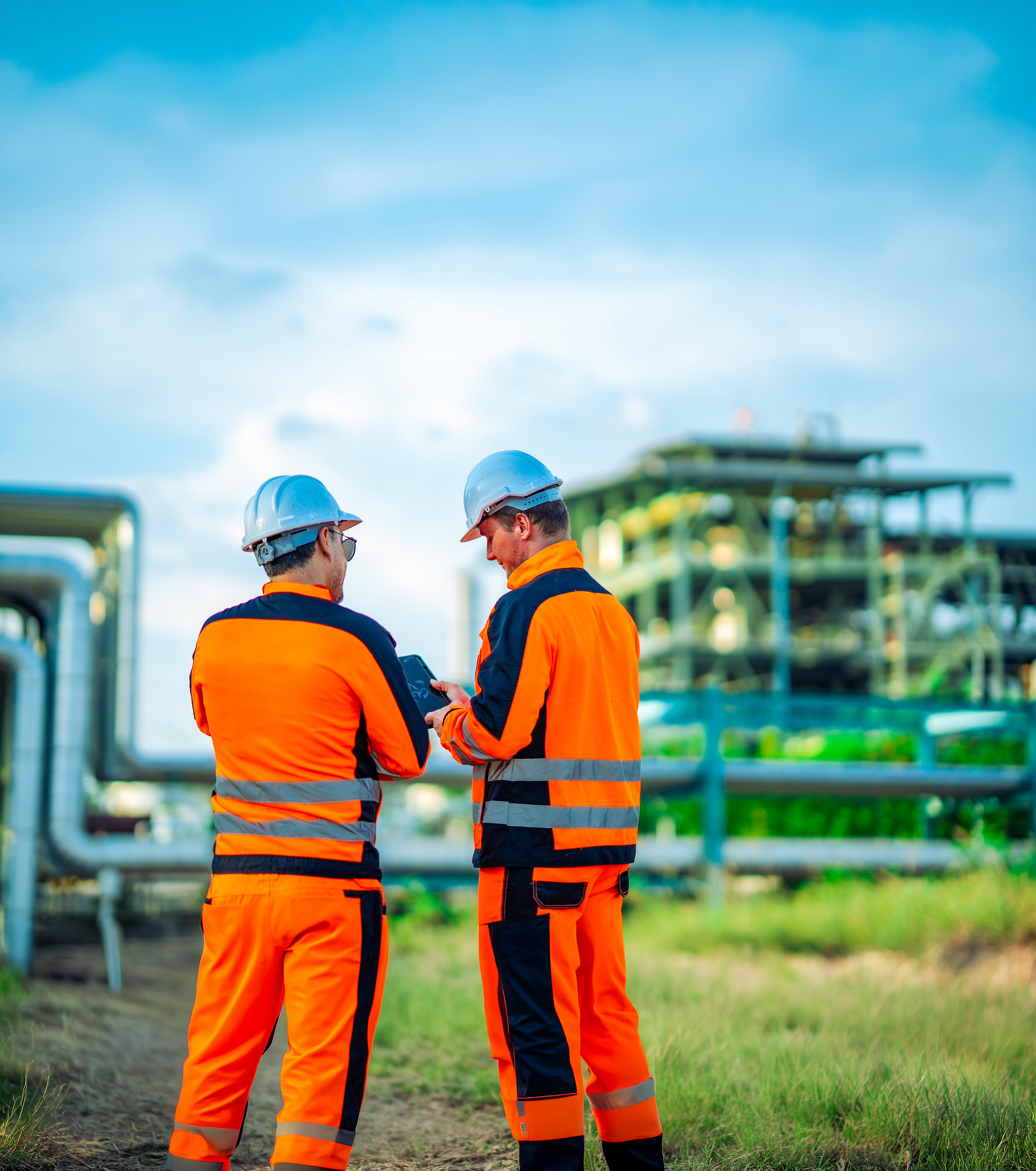 Two engineers observing refinery infrastructure from a production area during an industrial inspection. Facility monitoring, engineering collaboration, operational planning, energy industry, workplace safety.