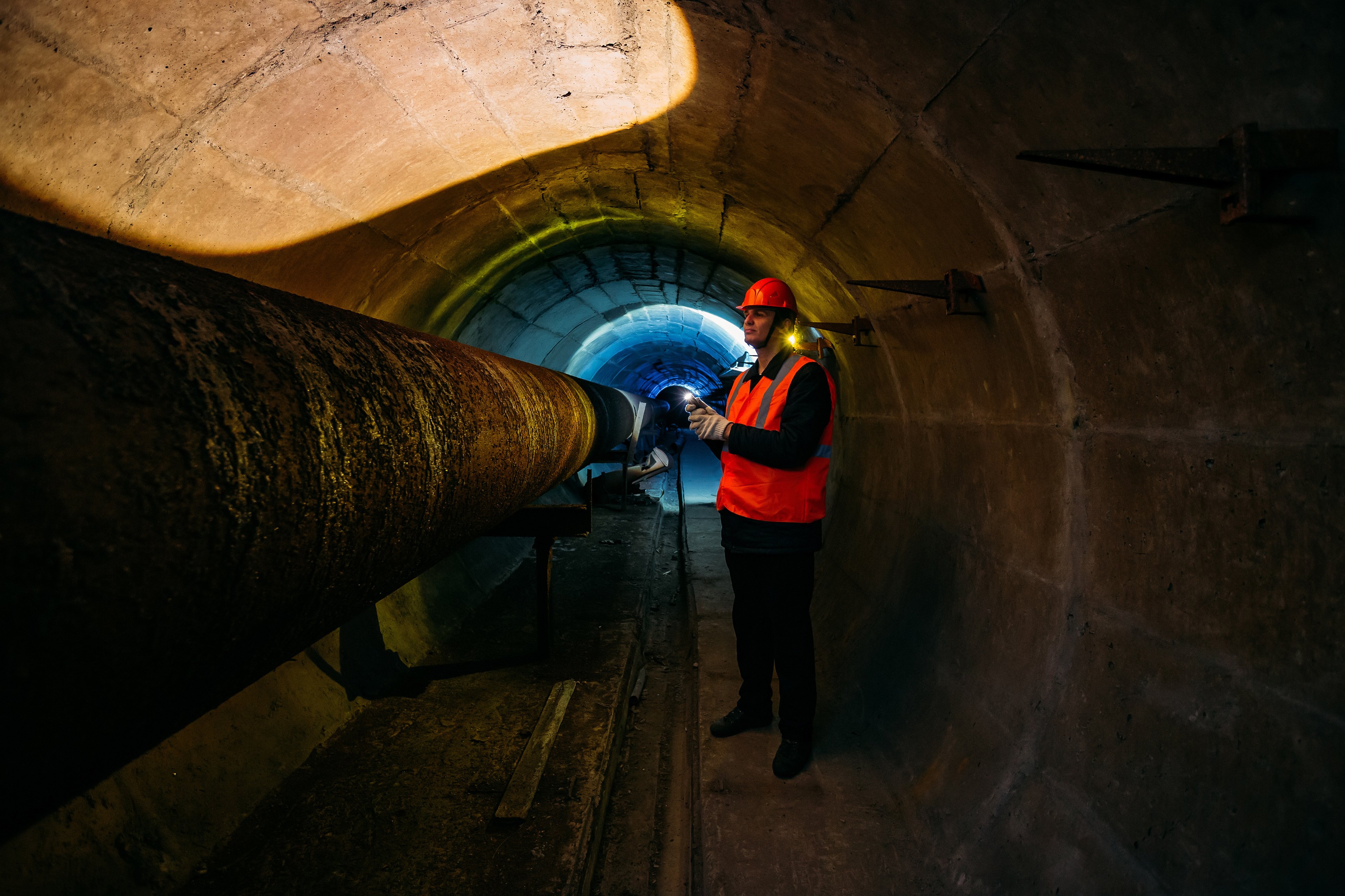 Tunnel worker examines pipeline in underground tunnel.