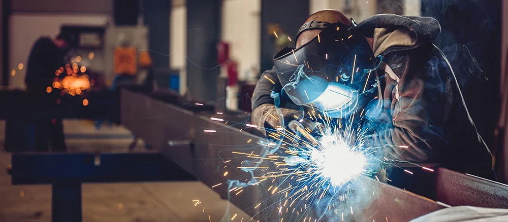 Industrial Welder With Torch and Protective Helmet in big hall welding metal profiles