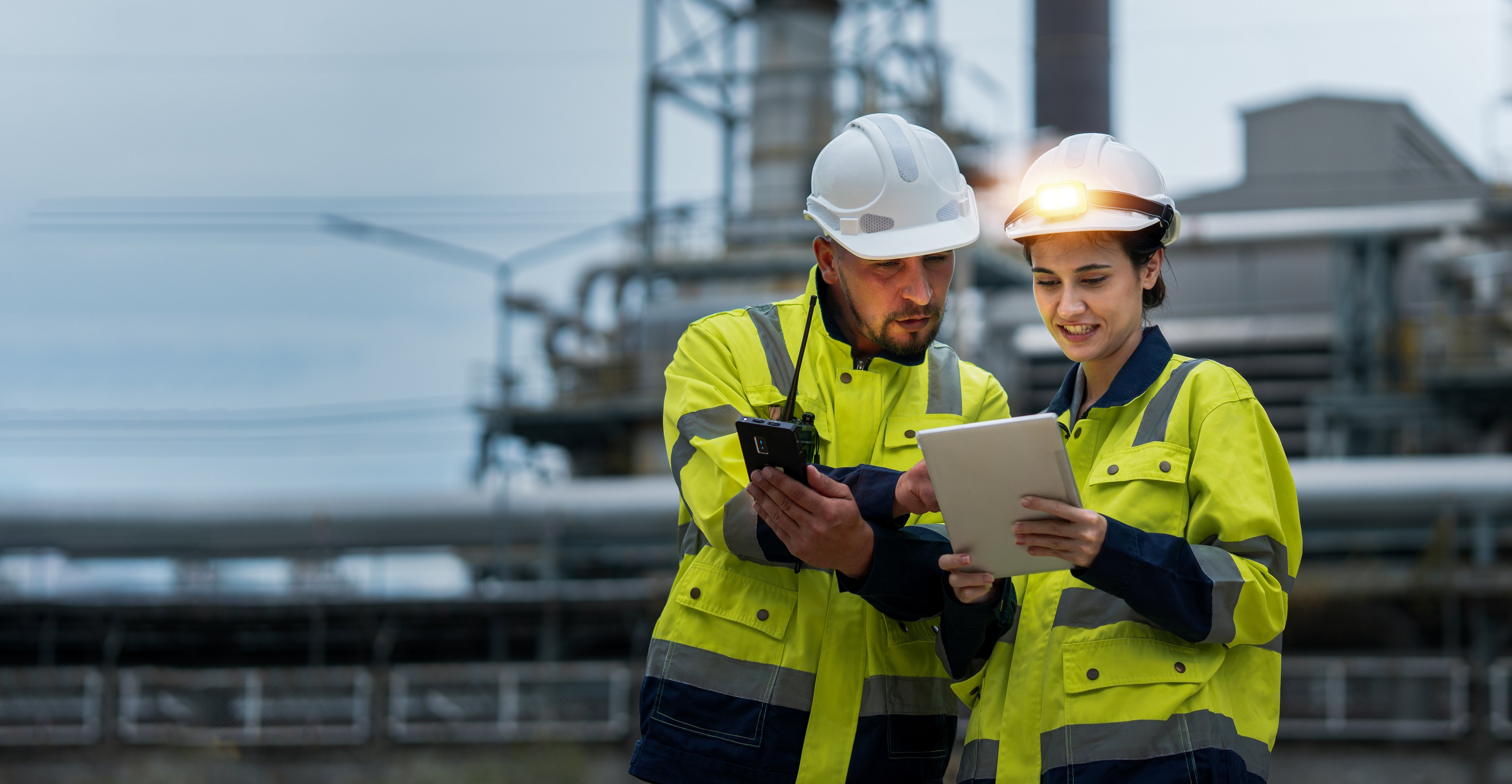 Male and female industrial engineers wearing hard hats talk to collaborate on new project. Team of engineers inspecting gas separation plant using tablets.
