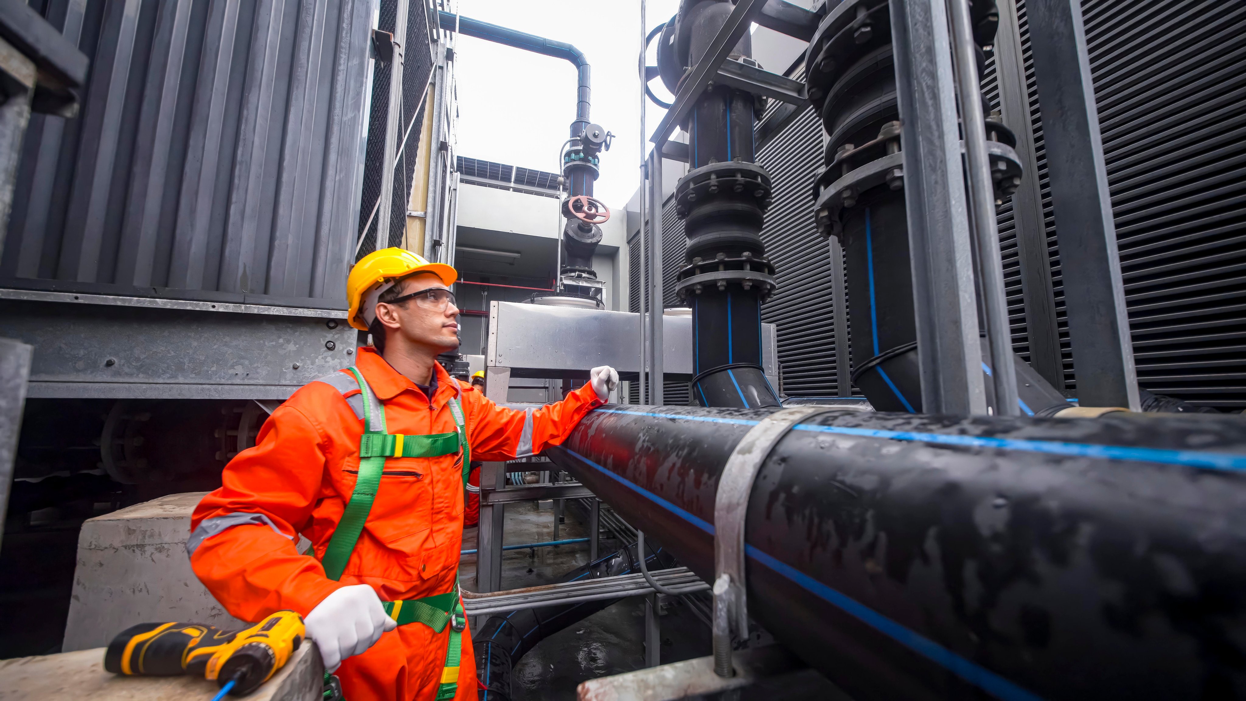 Worker examines large pipes at a power facility during daylight hours, ensuring safety.