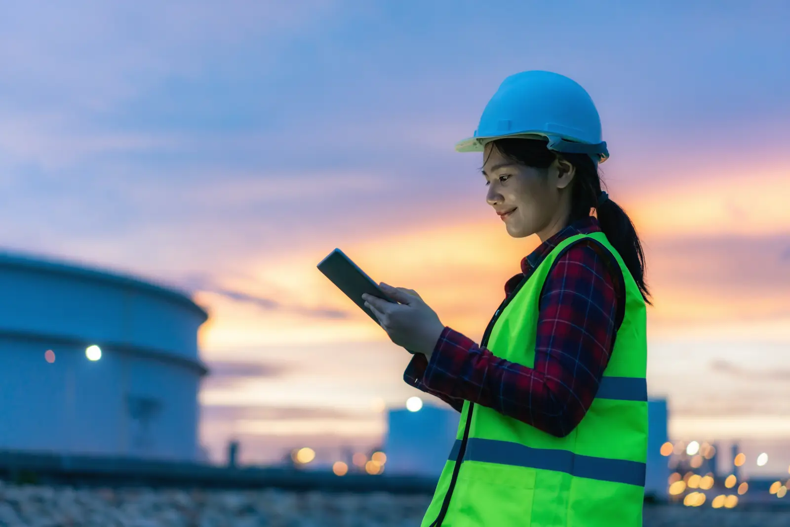 Asian woman petrochemical engineer working at night with digital tablet Inside oil and gas refinery plant industry factory at night for inspector safety quality control.