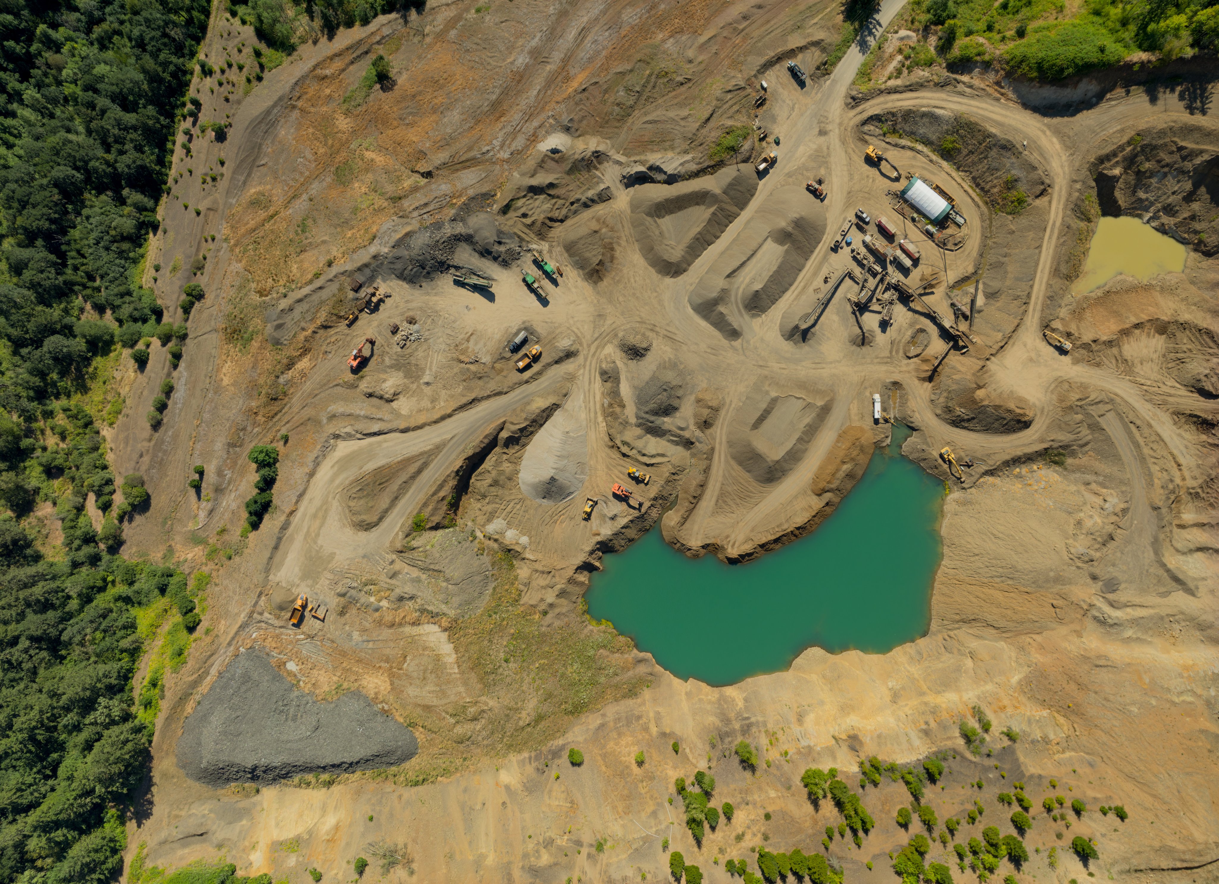 A large open pit mine with a large body of water in the middle. The water is green and the pit is surrounded by dirt and rocks
