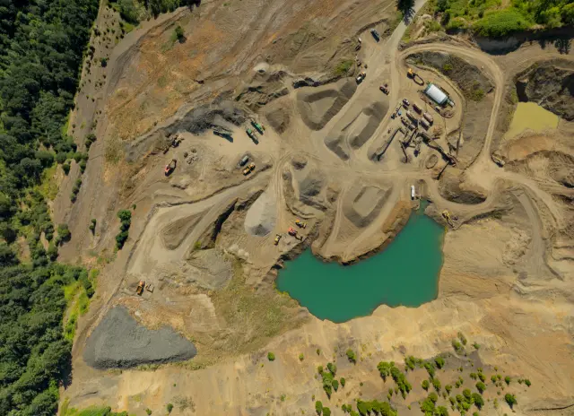 A large open pit mine with a large body of water in the middle. The water is green and the pit is surrounded by dirt and rocks