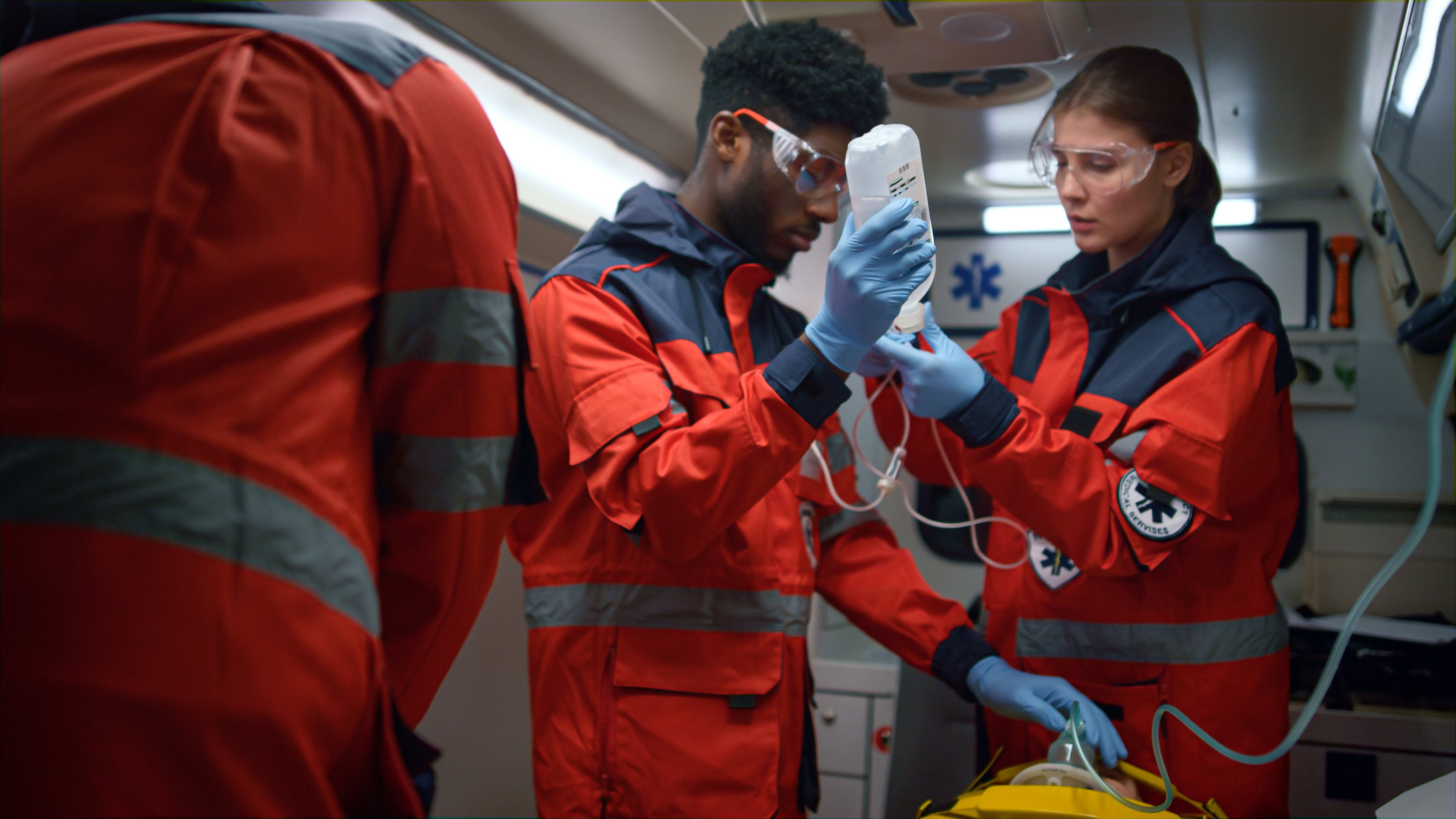 Professional paramedics performing first aid procedure in emergency car. Mixed race emergency doctors putting oxygen mask on man face. Ambulance crew talking care about patient on stretchers 