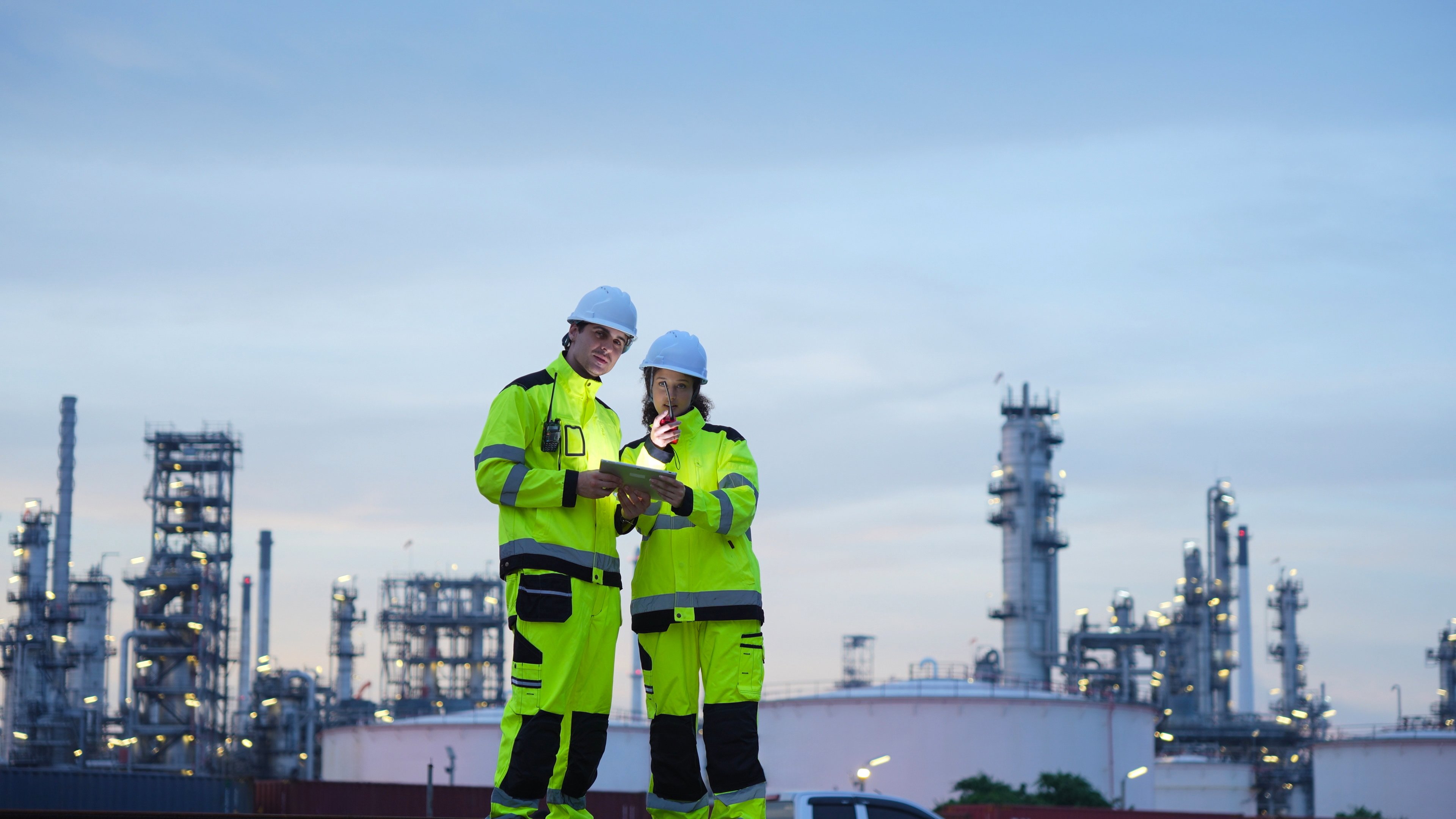 Engineers at an Industrial Plant at Dusk, Two Industrial Workers Collaborating On-Site, Professional Engineers Overseeing Operations at a Refinery