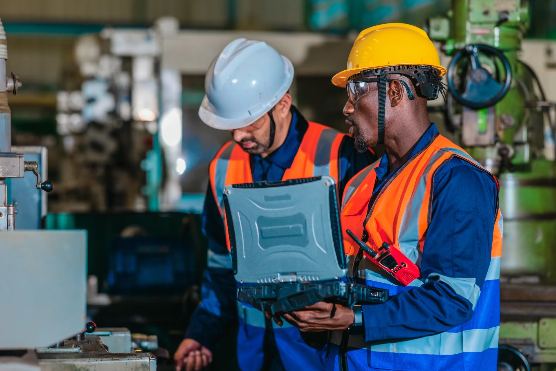 A supervisor mentors a technician using a rugged laptop beside a production machine in a manufacturing facility, showing digital supervision, faster troubleshooting, productivity, and process control.