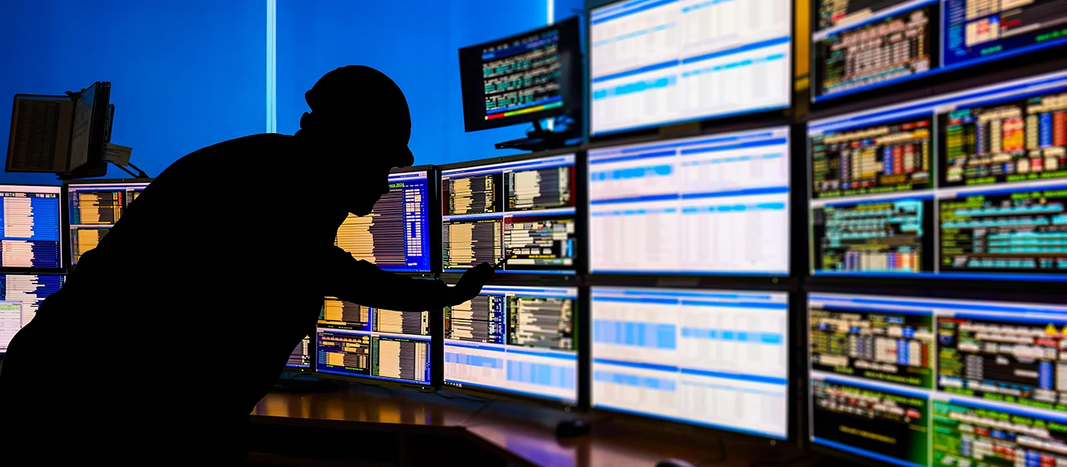 SCADA system in the central heating process.  Silhouette of an operator analyzing data on multiple monitors - ensuring optimal performance and safety in industrial automation systems.