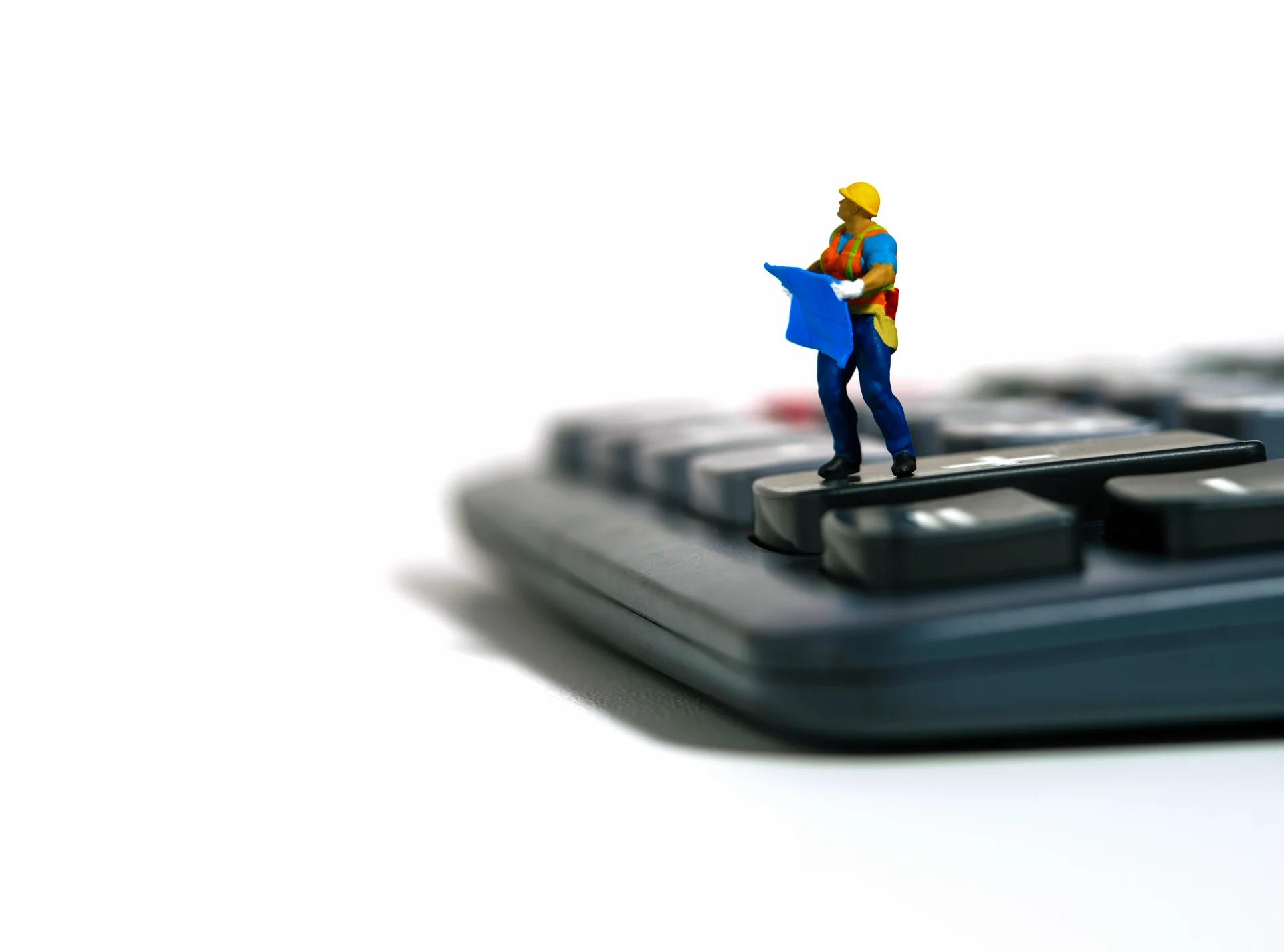 Miniature people toy figure photography. Project budget cost calculation concept. A construction worker with blueprint building standing above calculator. Isolated on white background. Image photo