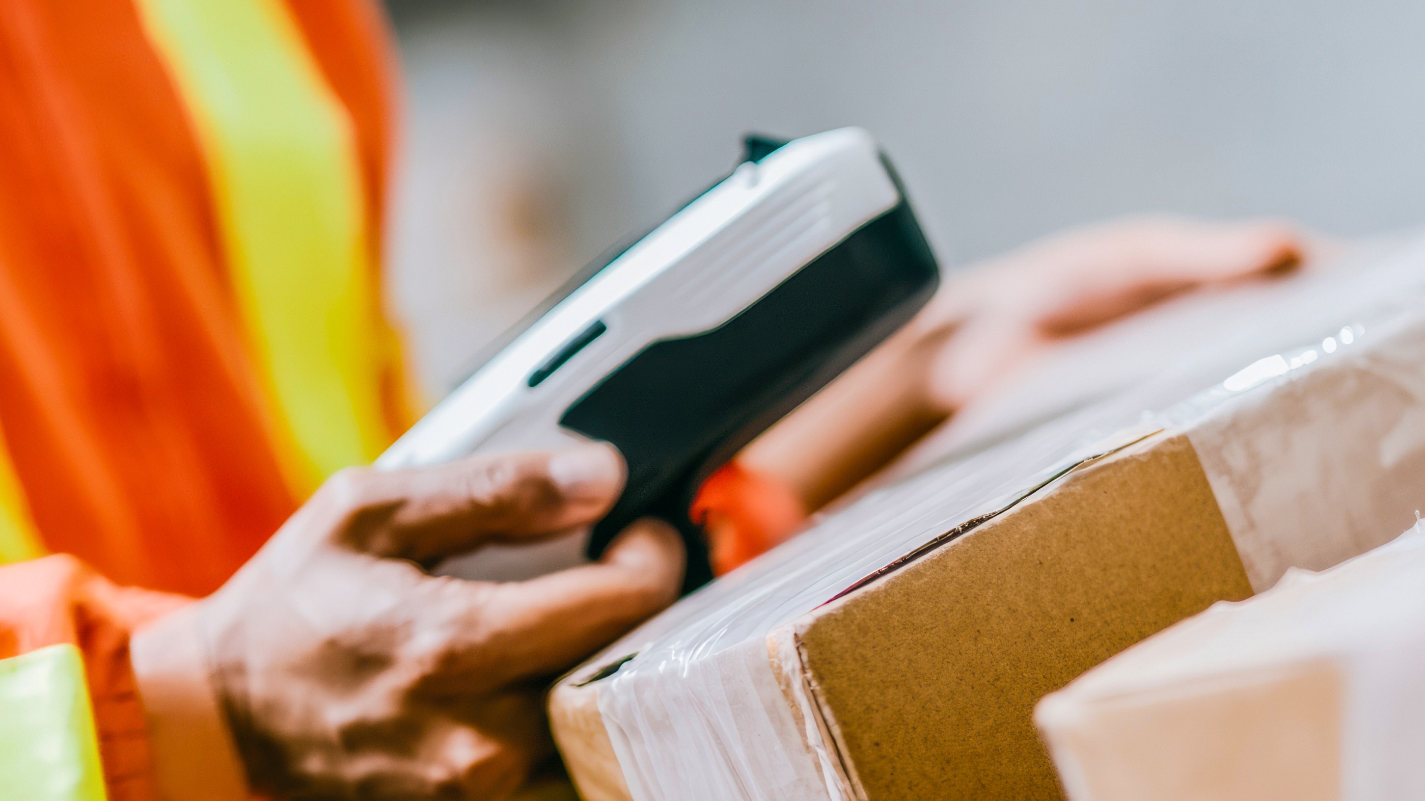 Warehouse worker scanning cardboard boxes using a portable barcode scanner for inventory management in a modern logistics facility with storage background and copy space.