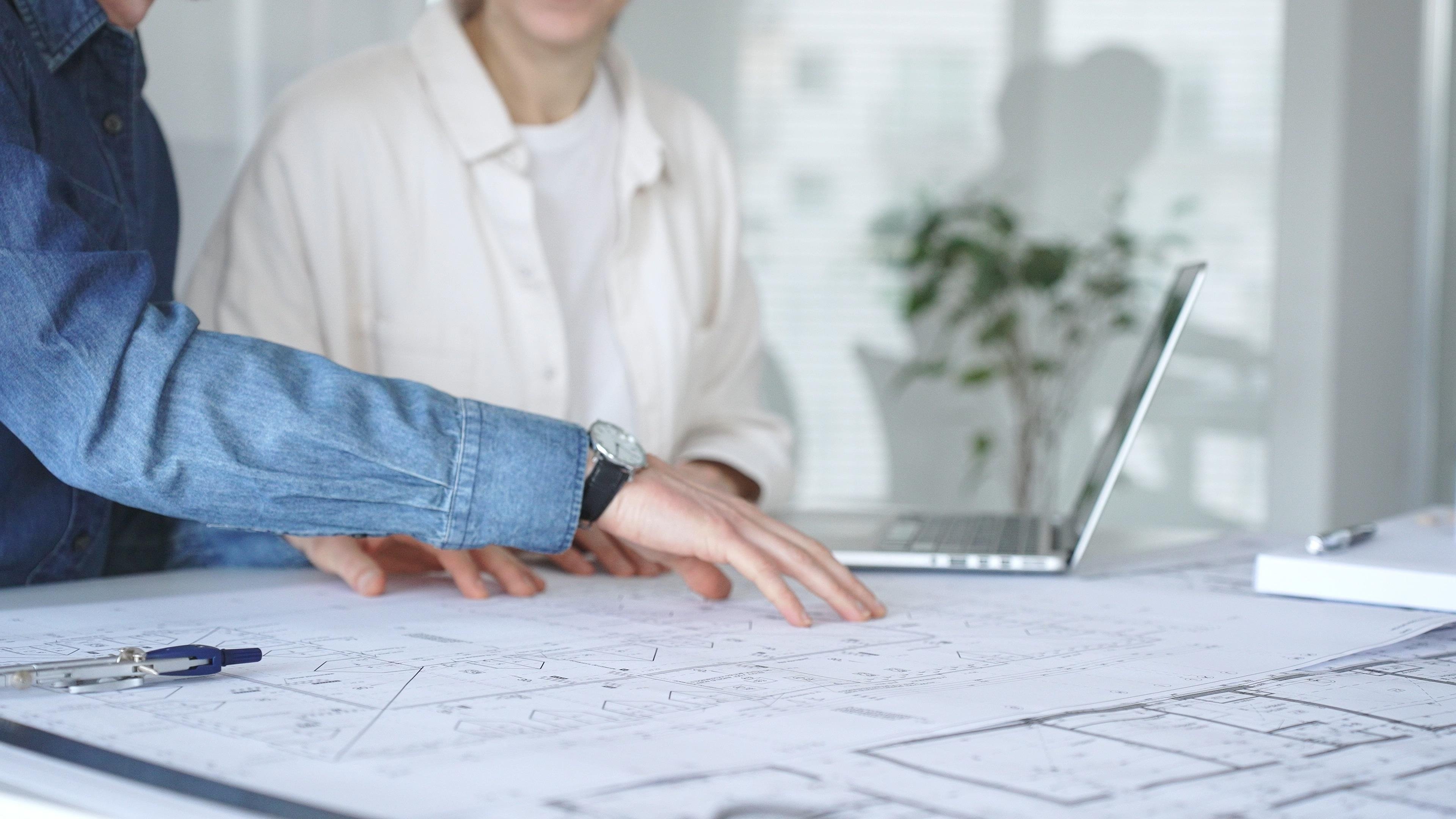 Architectural professionals reviewing blueprints on a desk with a laptop, engaging in a focused discussion about design concepts and project development in an modern office environment