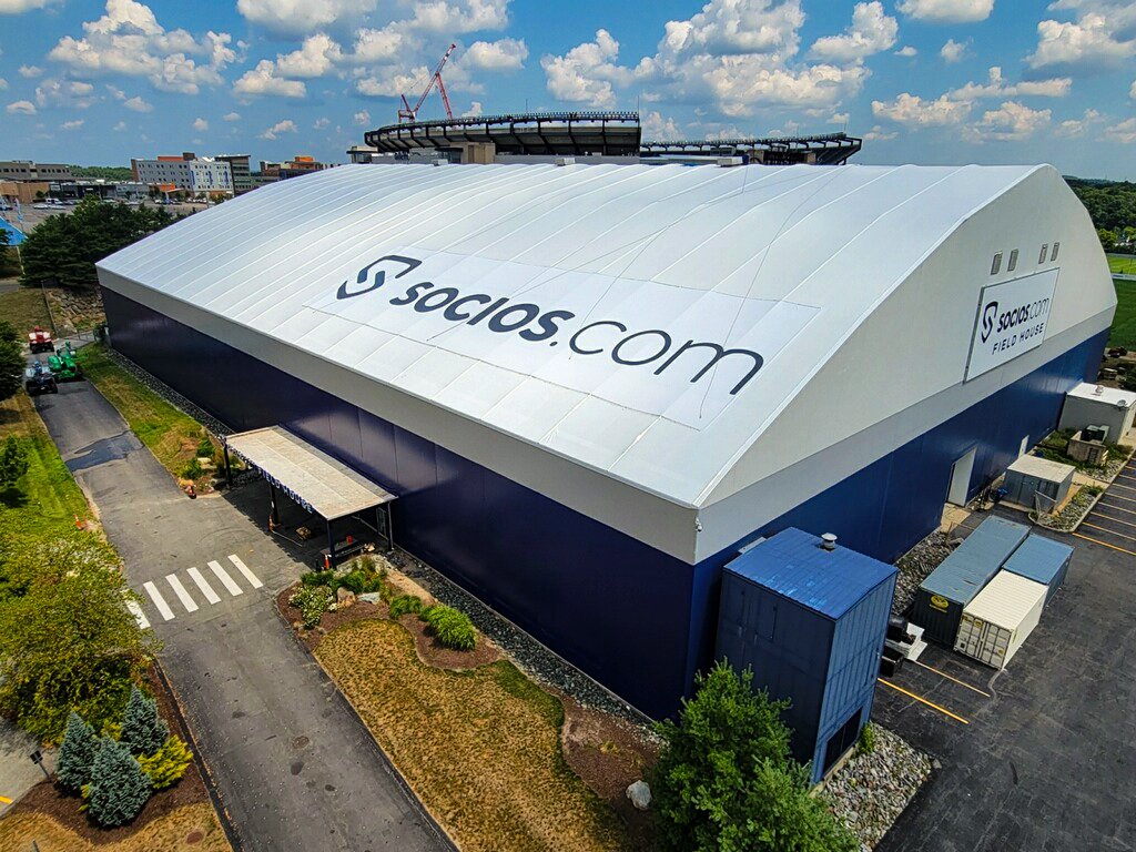 Aerial view of a large clearspan fabric building with a company logo printed across its white roof