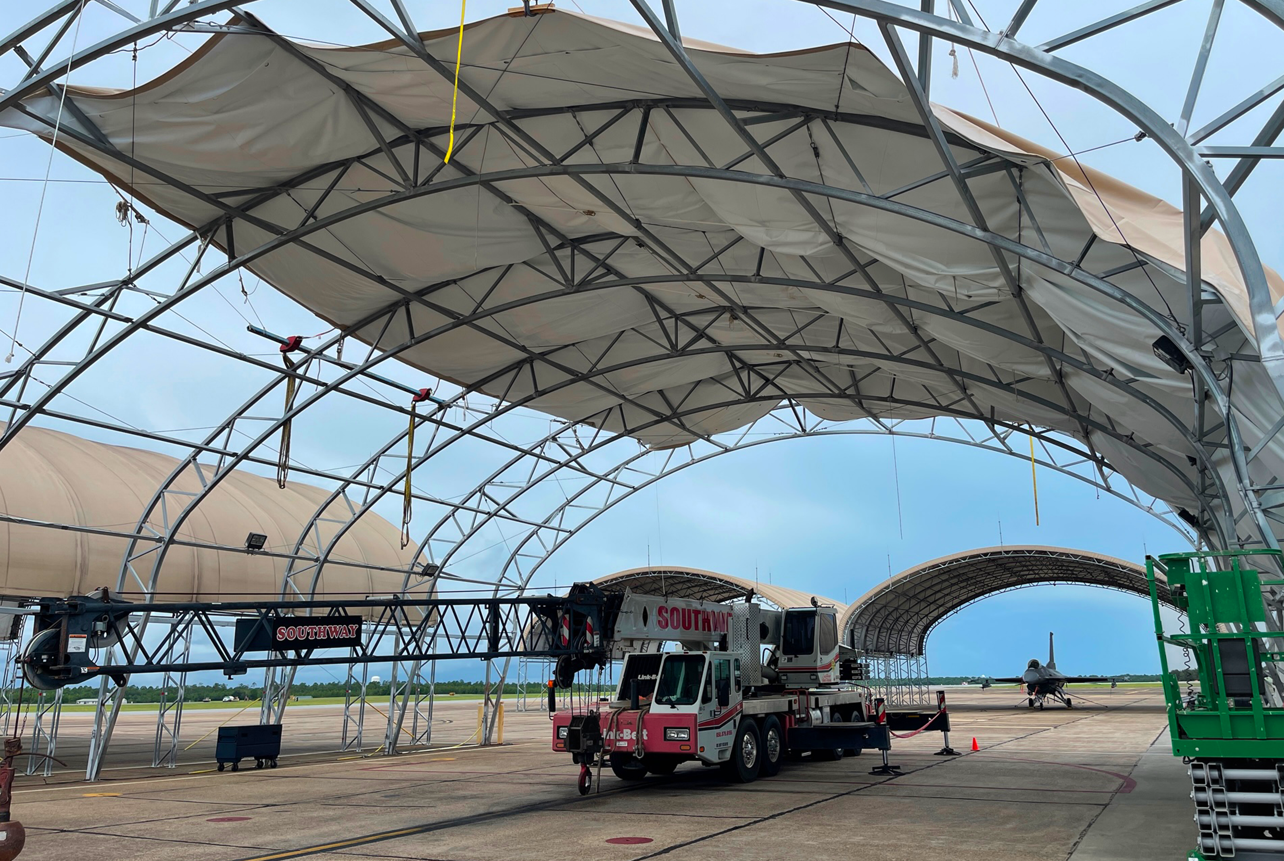 Steel arch hangar frame with a loose fabric cover overhead and a crane parked beneath it